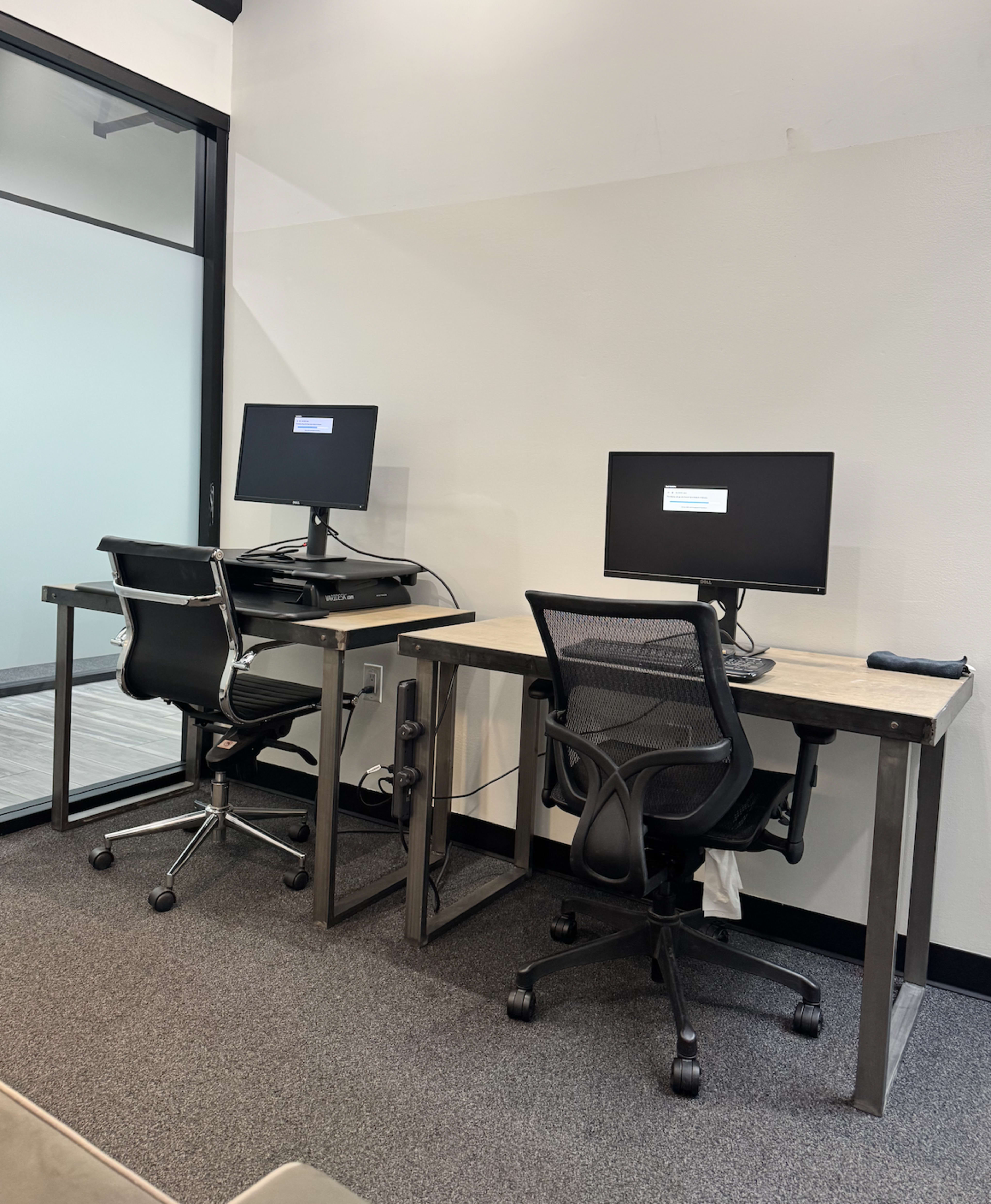 The image shows two desks with computer monitors positioned in a small office space.