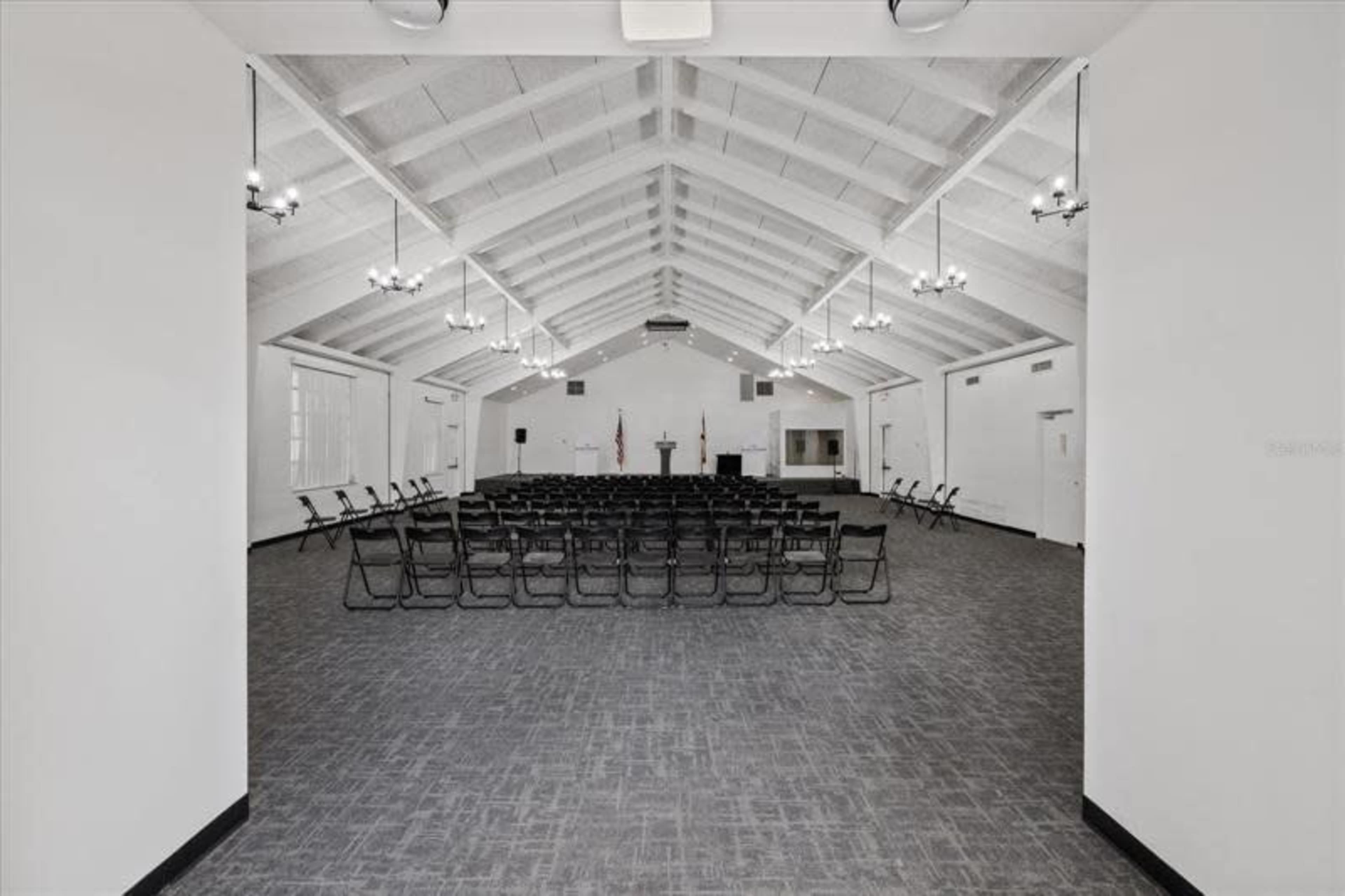 The image shows a large, empty hall with rows of chairs set up facing a podium under a high, vaulted ceiling.