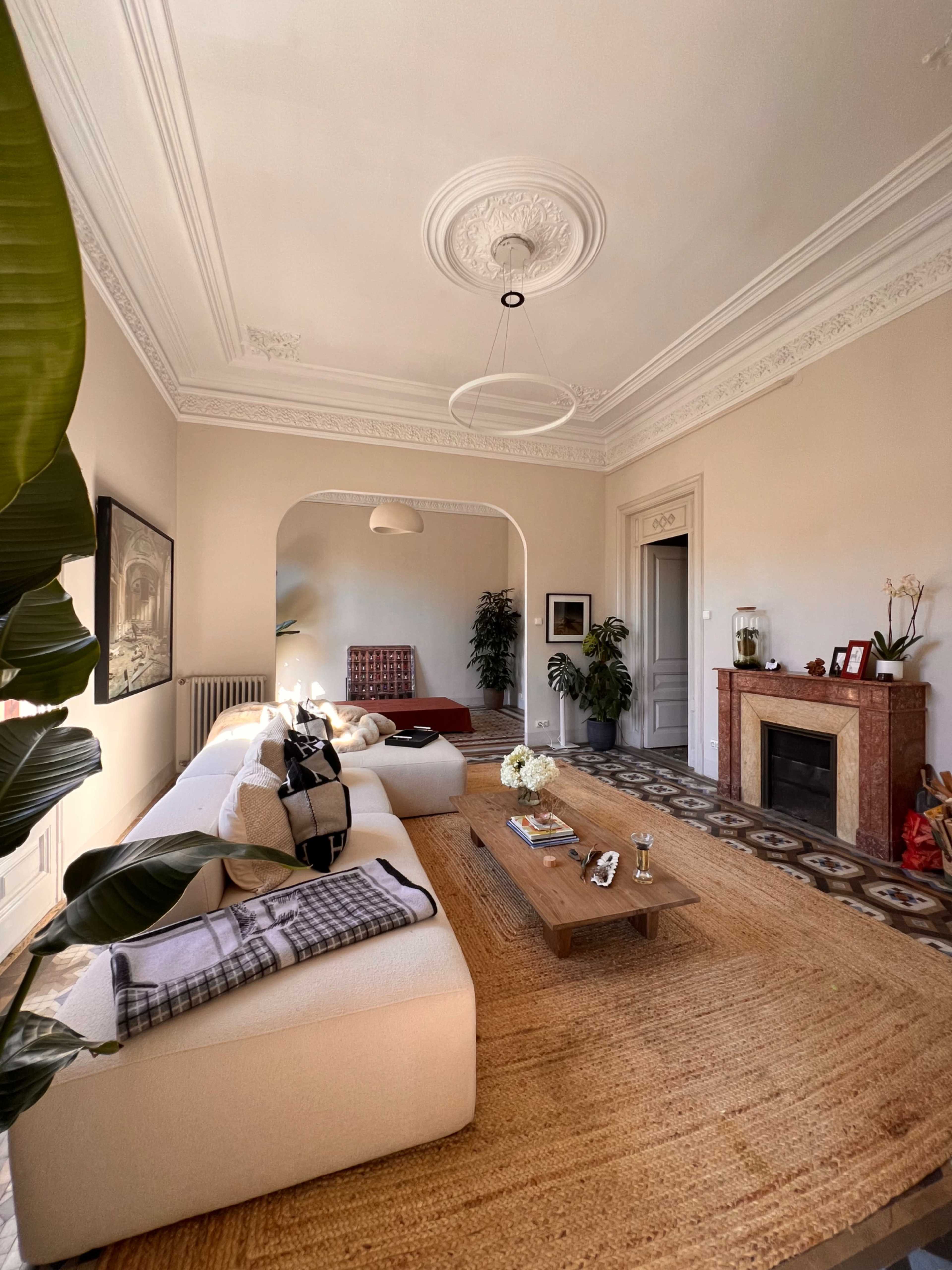 The image depicts a well-lit living room featuring a white sectional sofa, a wooden coffee table, and a fireplace adorned with decorative items.