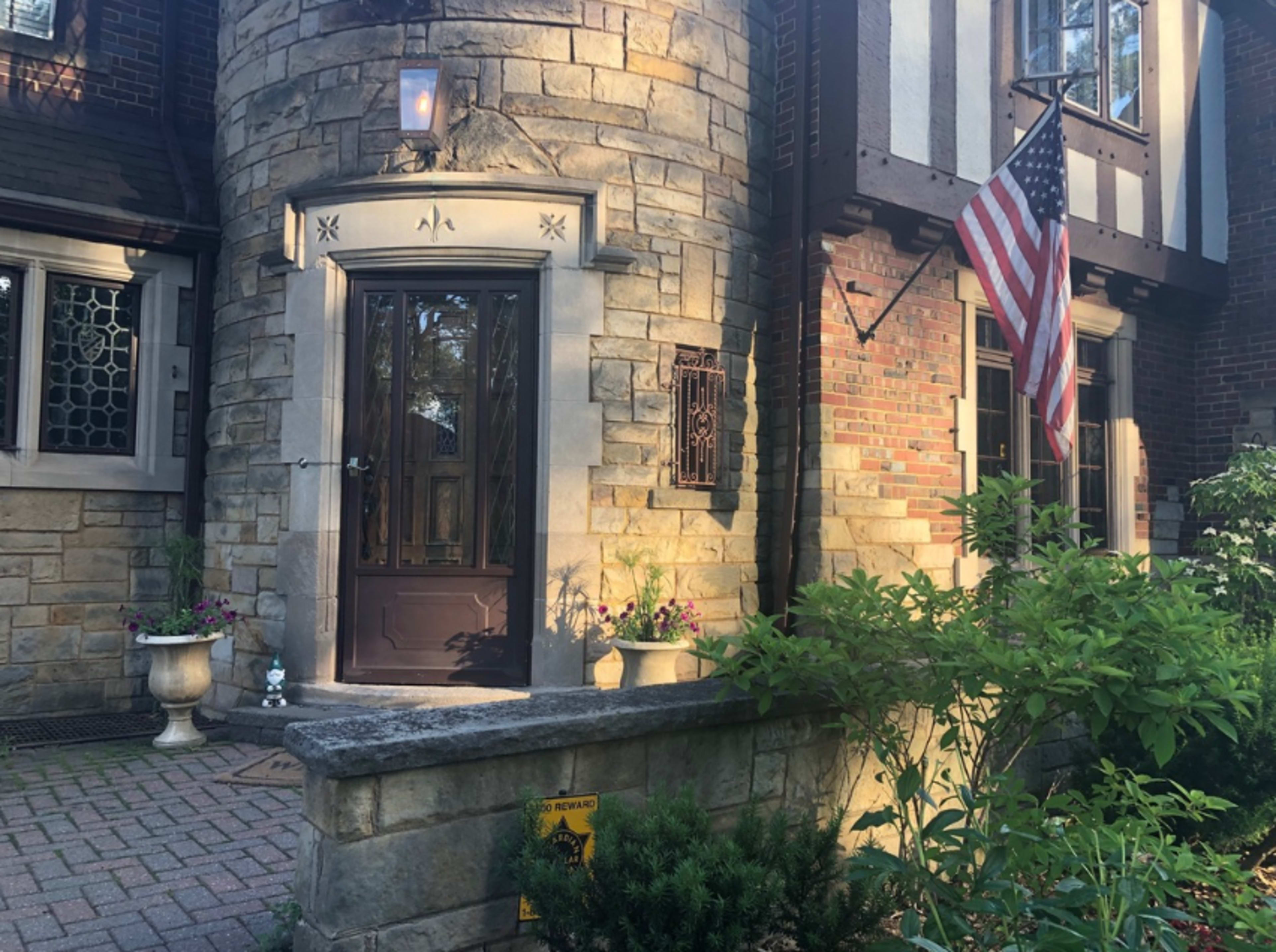 The entrance of a stone and brick house with a wooden front door and a U.S. flag displayed beside it.