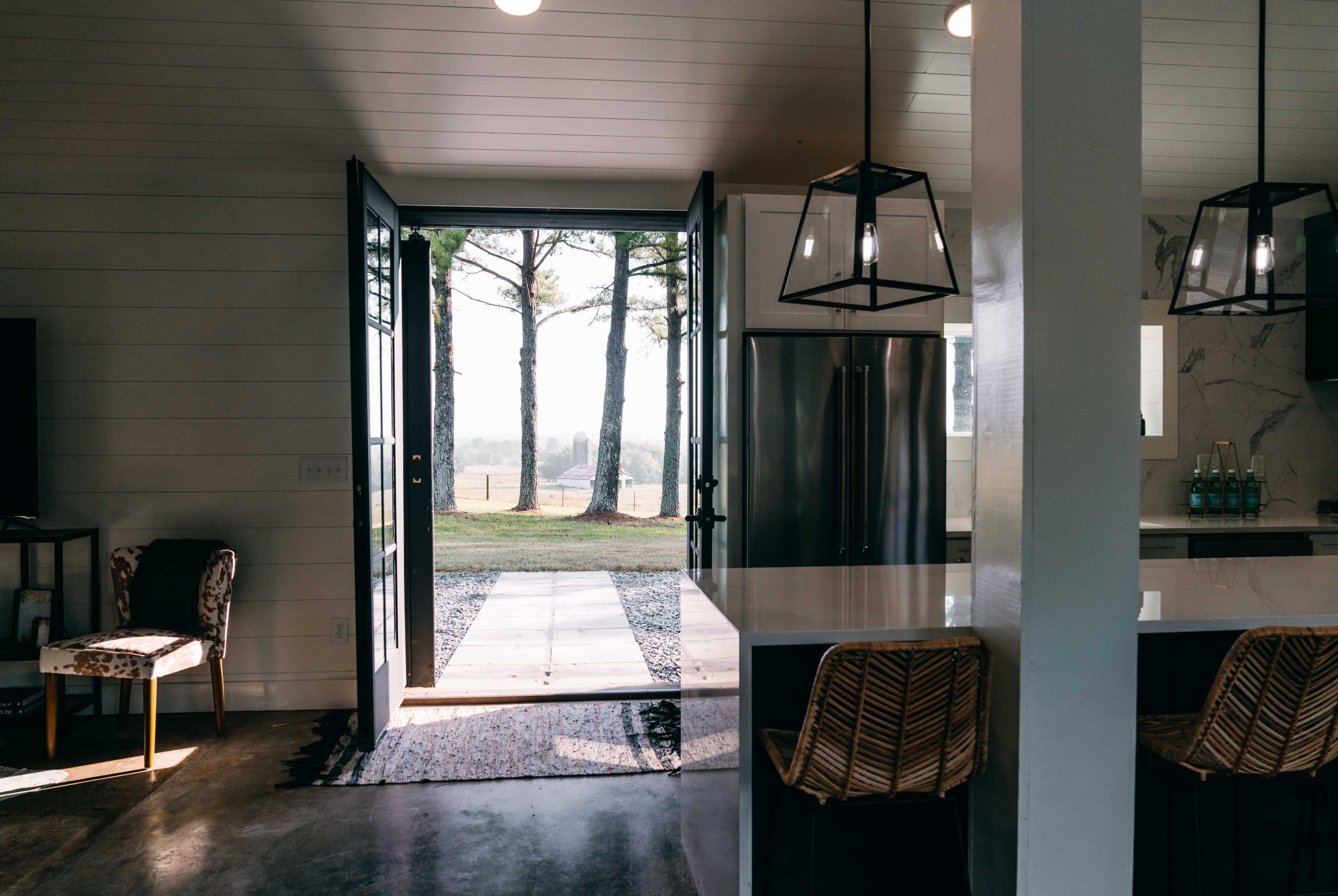 A modern kitchen opens to a doorway leading to a view of trees and greenery outside.