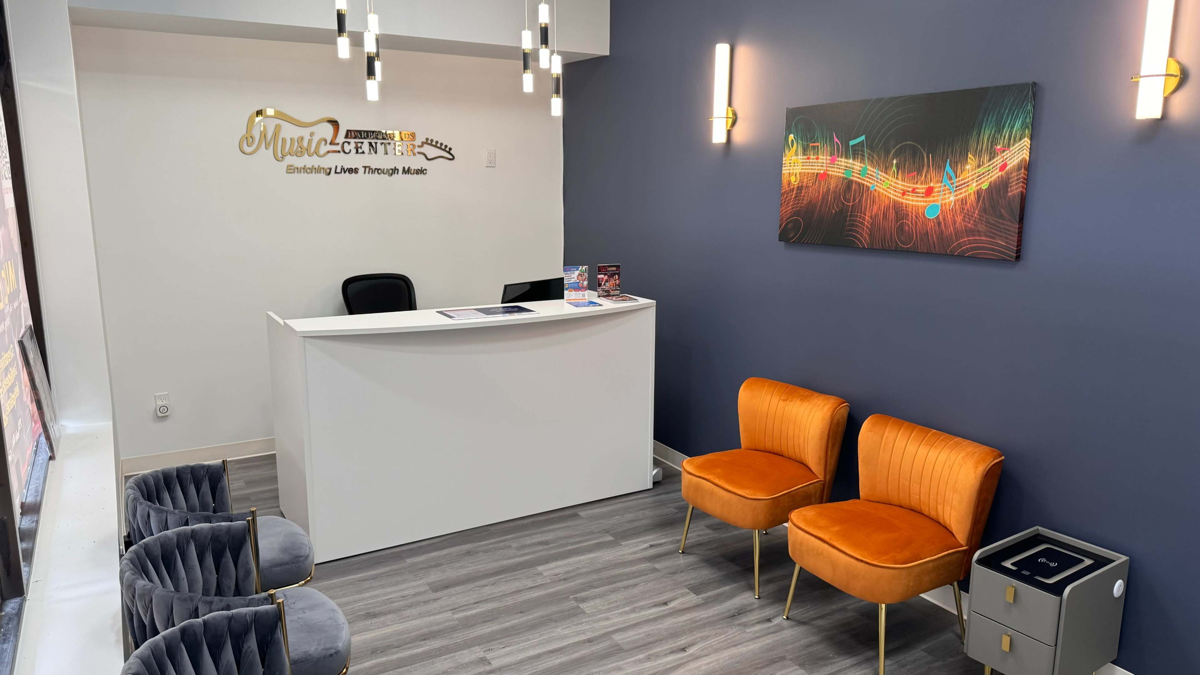 A modern reception area for "Music-Center," featuring a sleek white desk, orange chairs, and a colorful wall art display.
