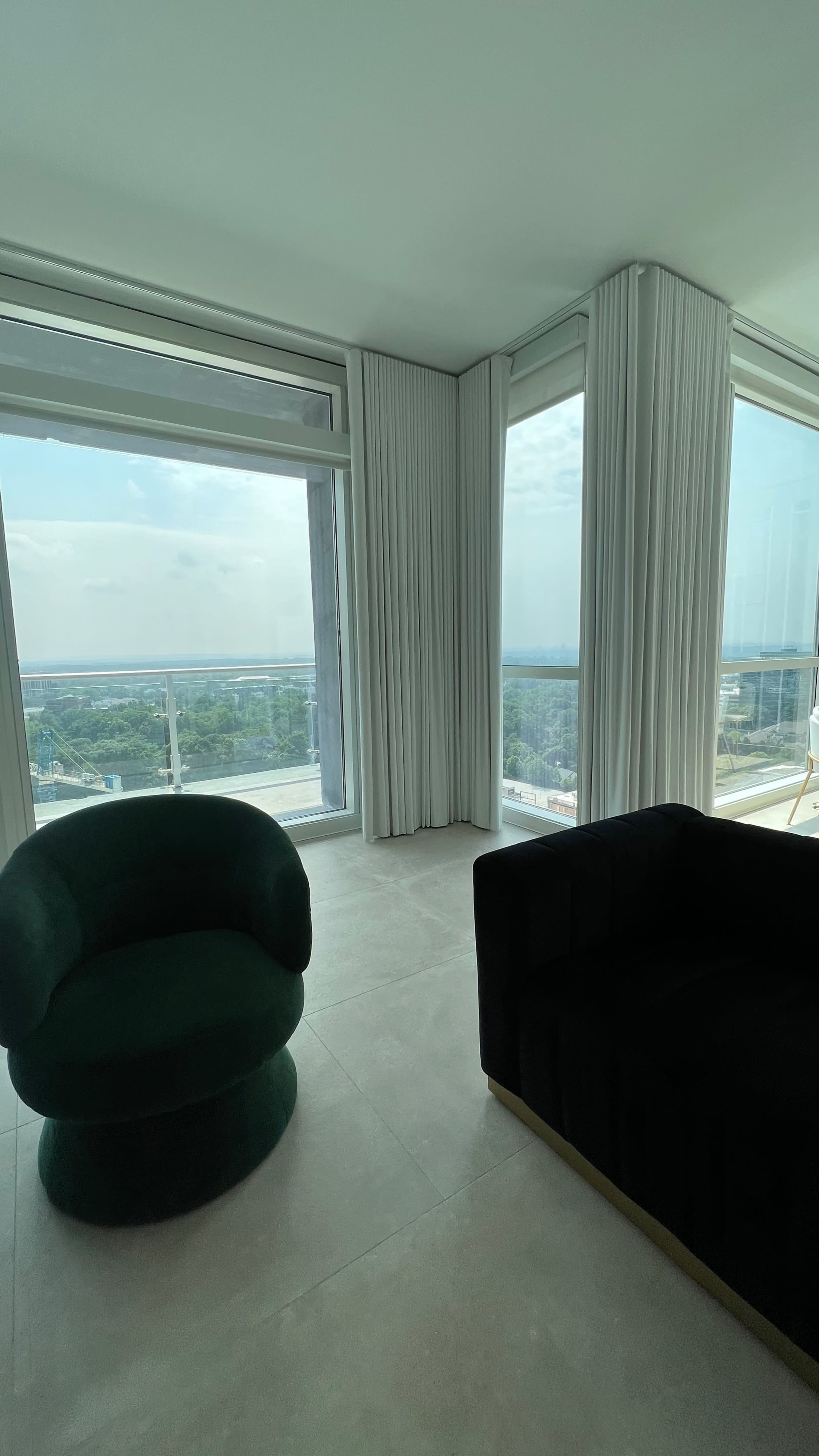The image shows a modern living room with two distinct sofas, one green and one black, near large windows with a view of the outdoors.