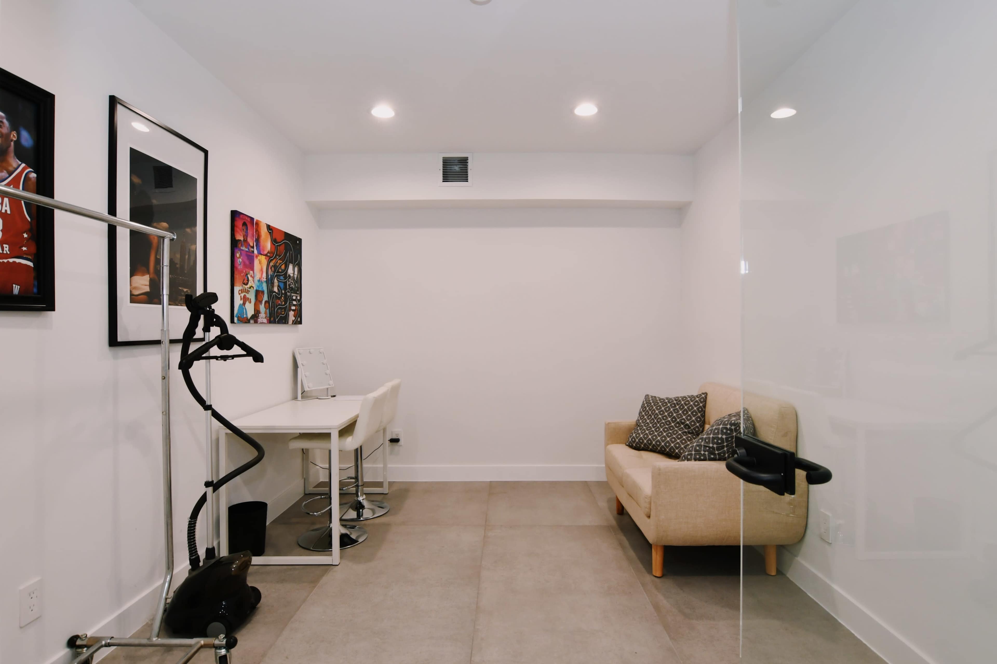 A modern room with a glass wall, featuring a small table with chairs, a couch, and wall art.