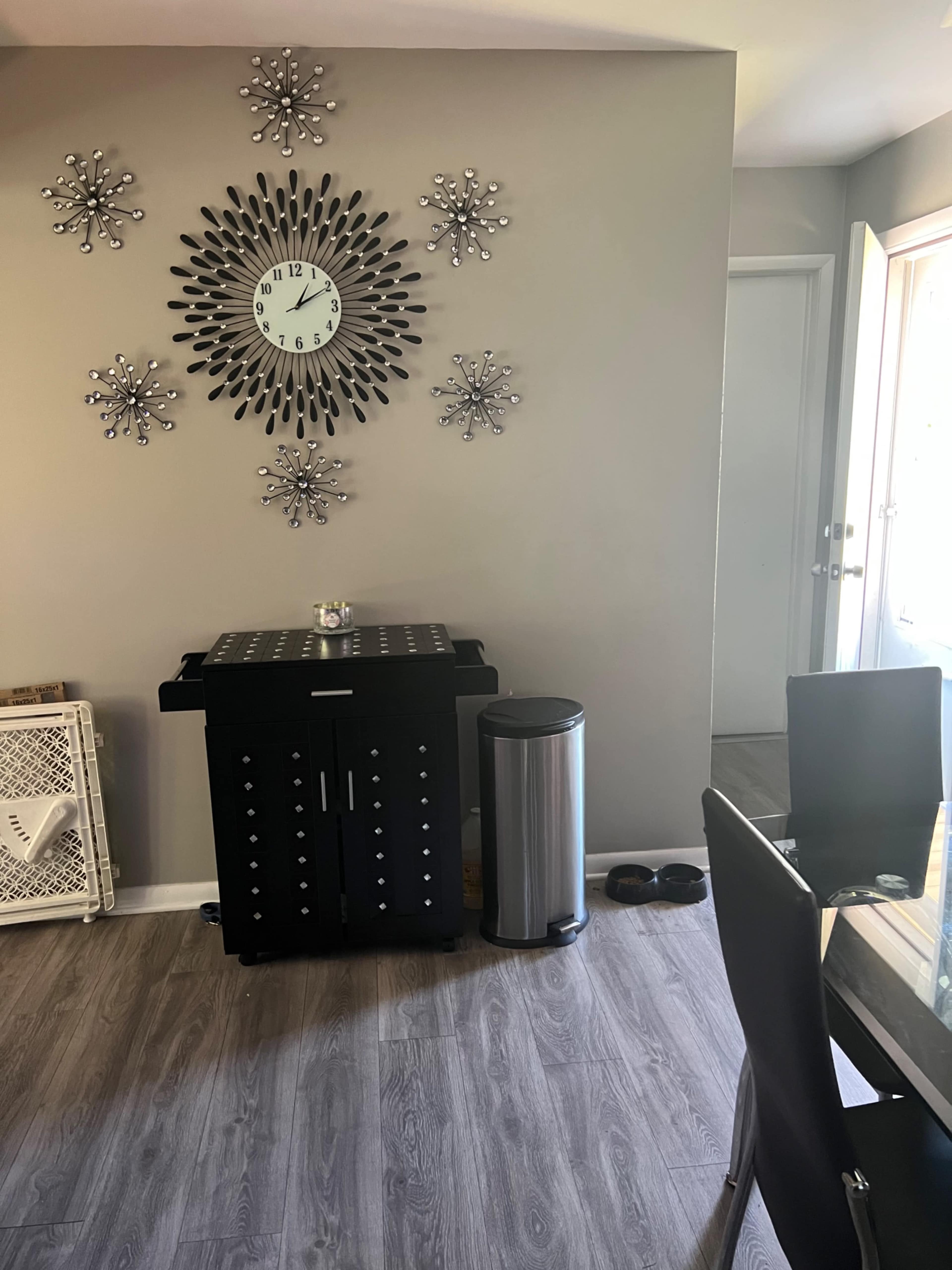 A modern dining area featuring a black cabinet, a silver trash can, a decorative wall clock, and star-shaped wall decorations.