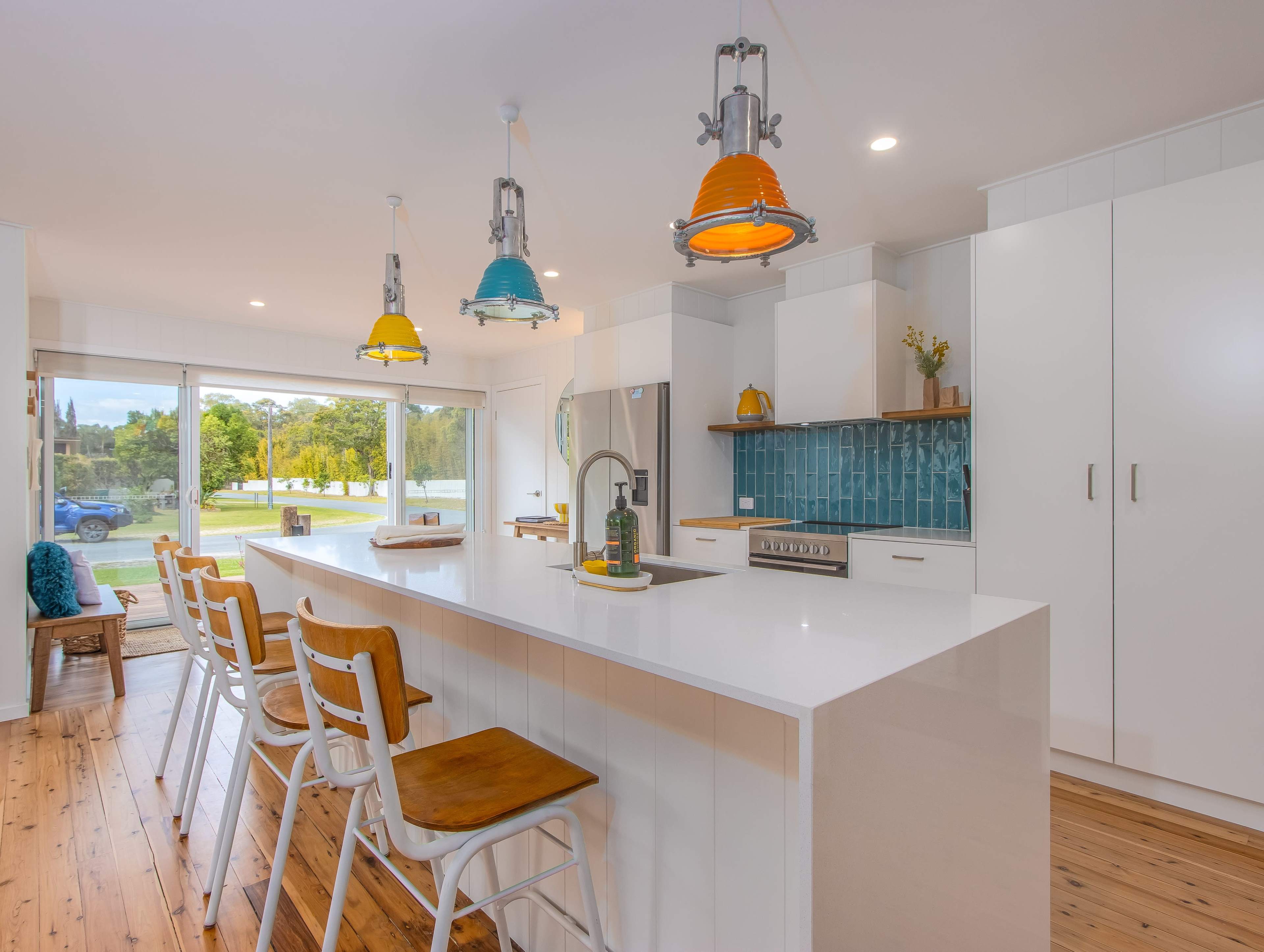 A modern kitchen with white cabinetry, a large island with bar seating, and colorful pendant lights hanging from the ceiling.