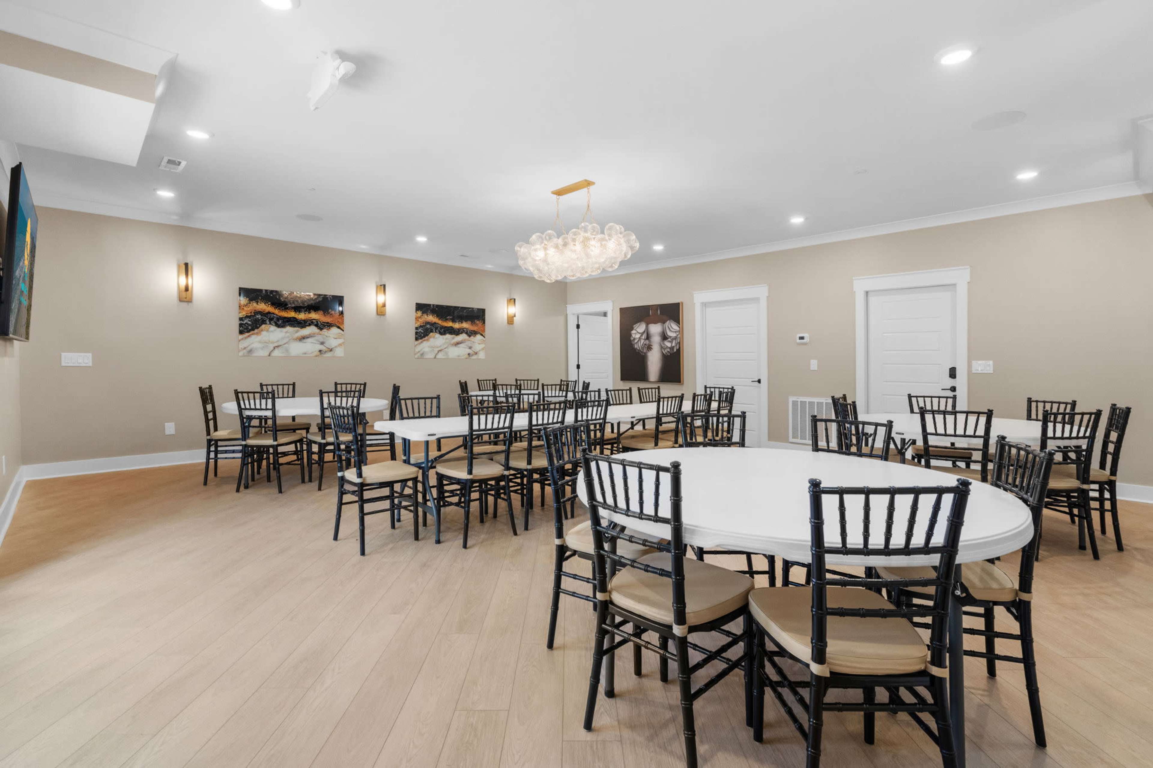 A large, well-lit room features several round tables surrounded by black chairs, with artwork adorning the walls.