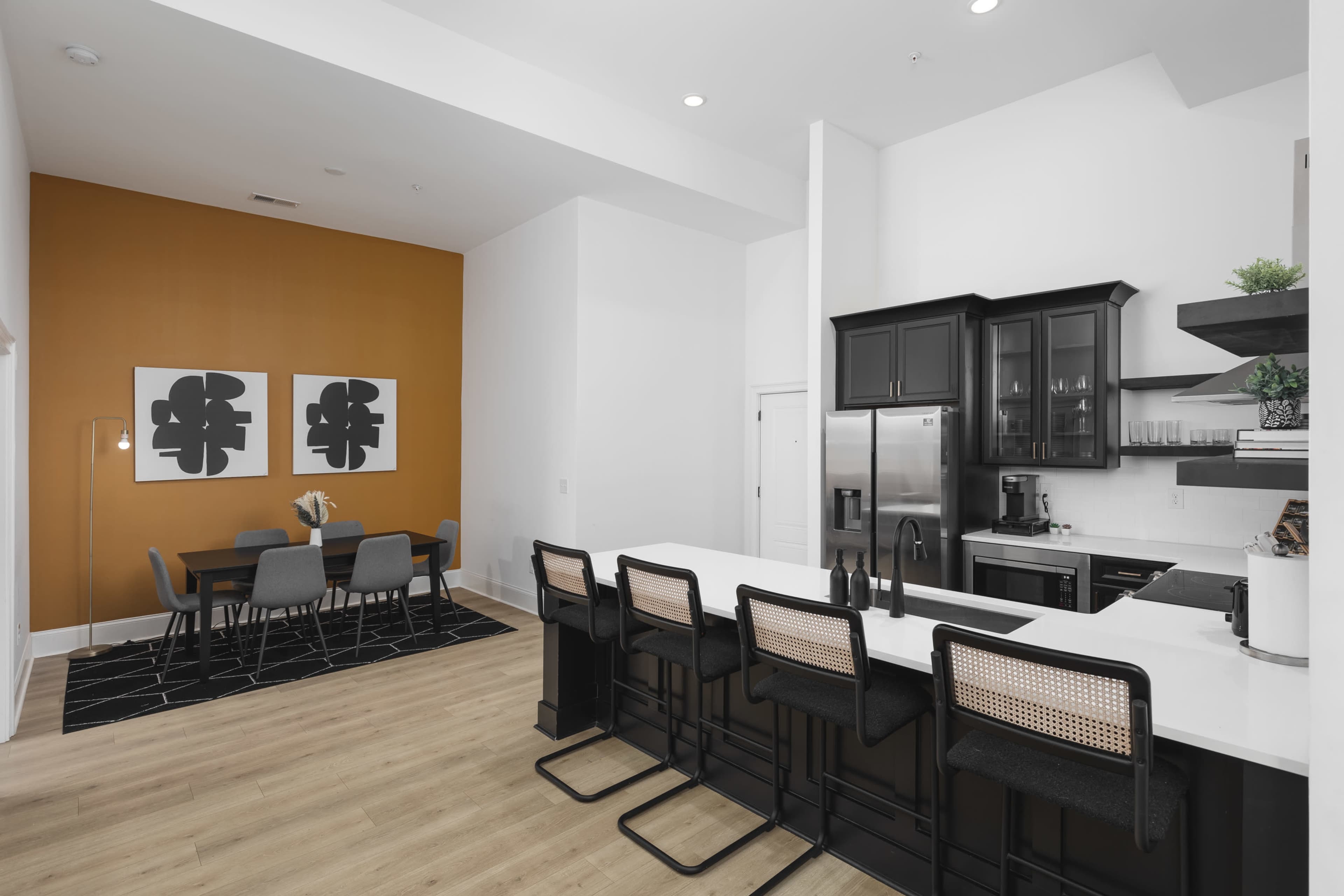 The image shows a modern kitchen and dining area with black cabinetry, a white island, and a dining table set against an orange feature wall.