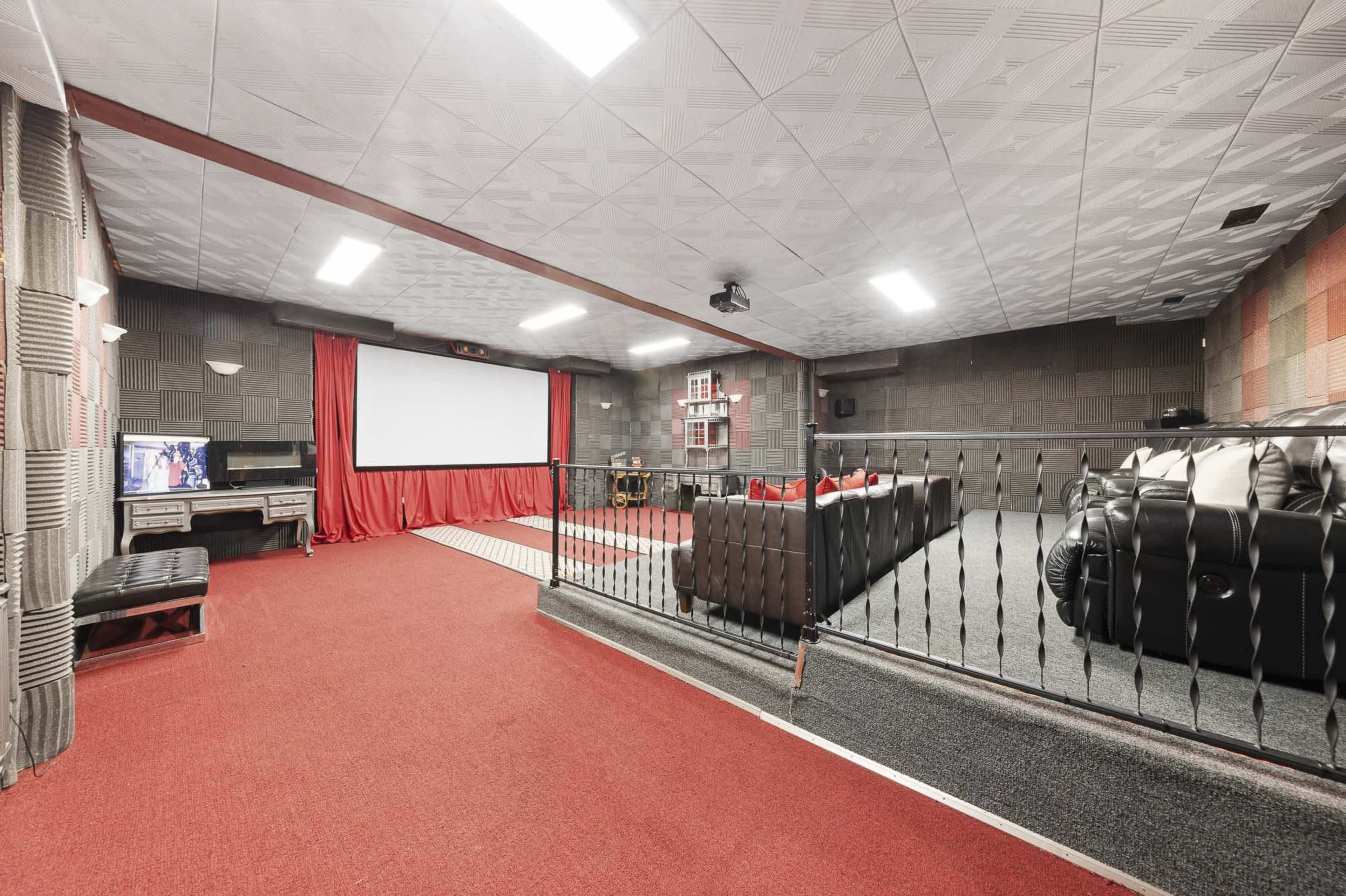 A home theater room with a large screen, comfortable seating, and red curtains.