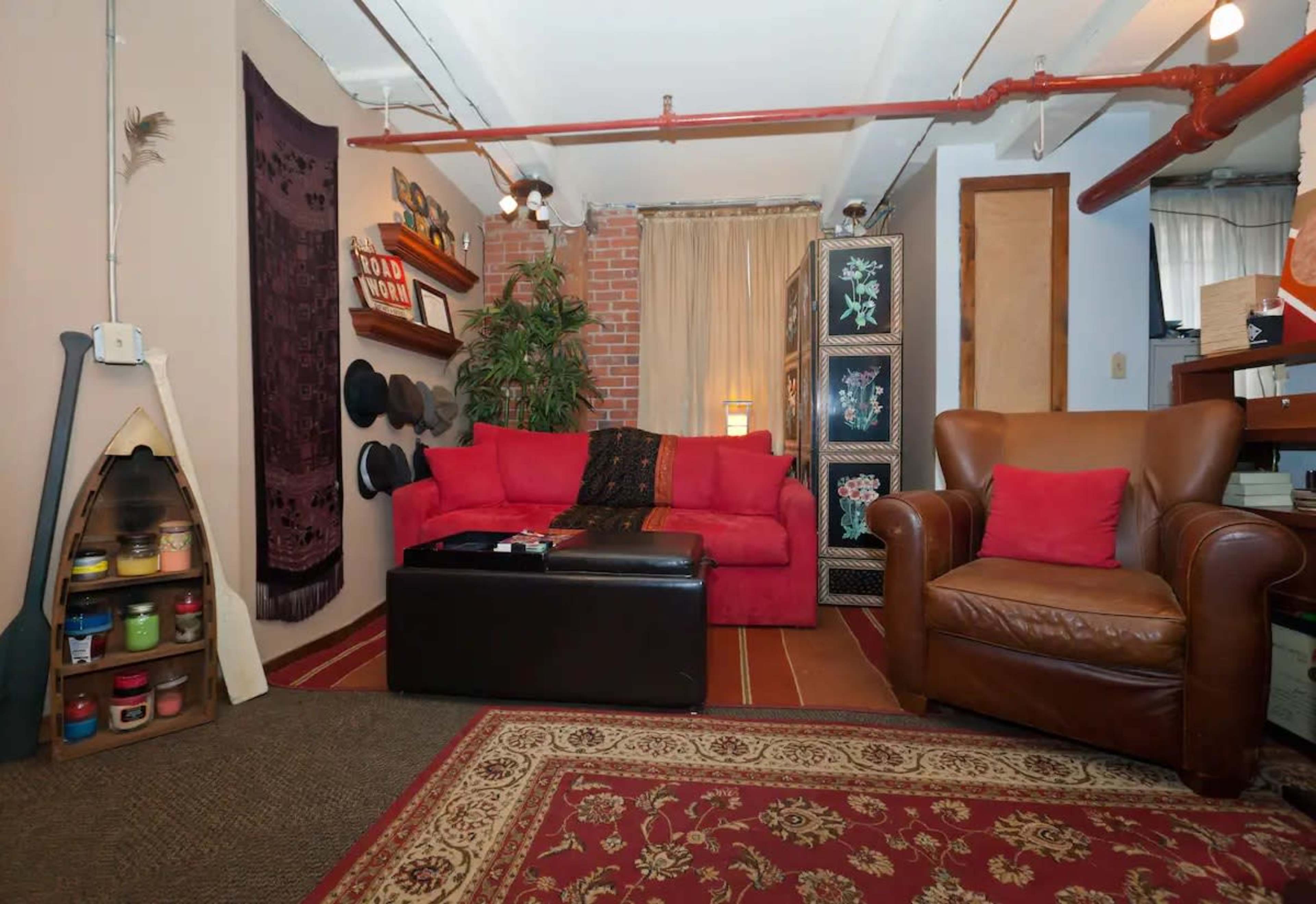 The room features a red couch, a brown leather armchair, and decorative elements including plants and wall art.