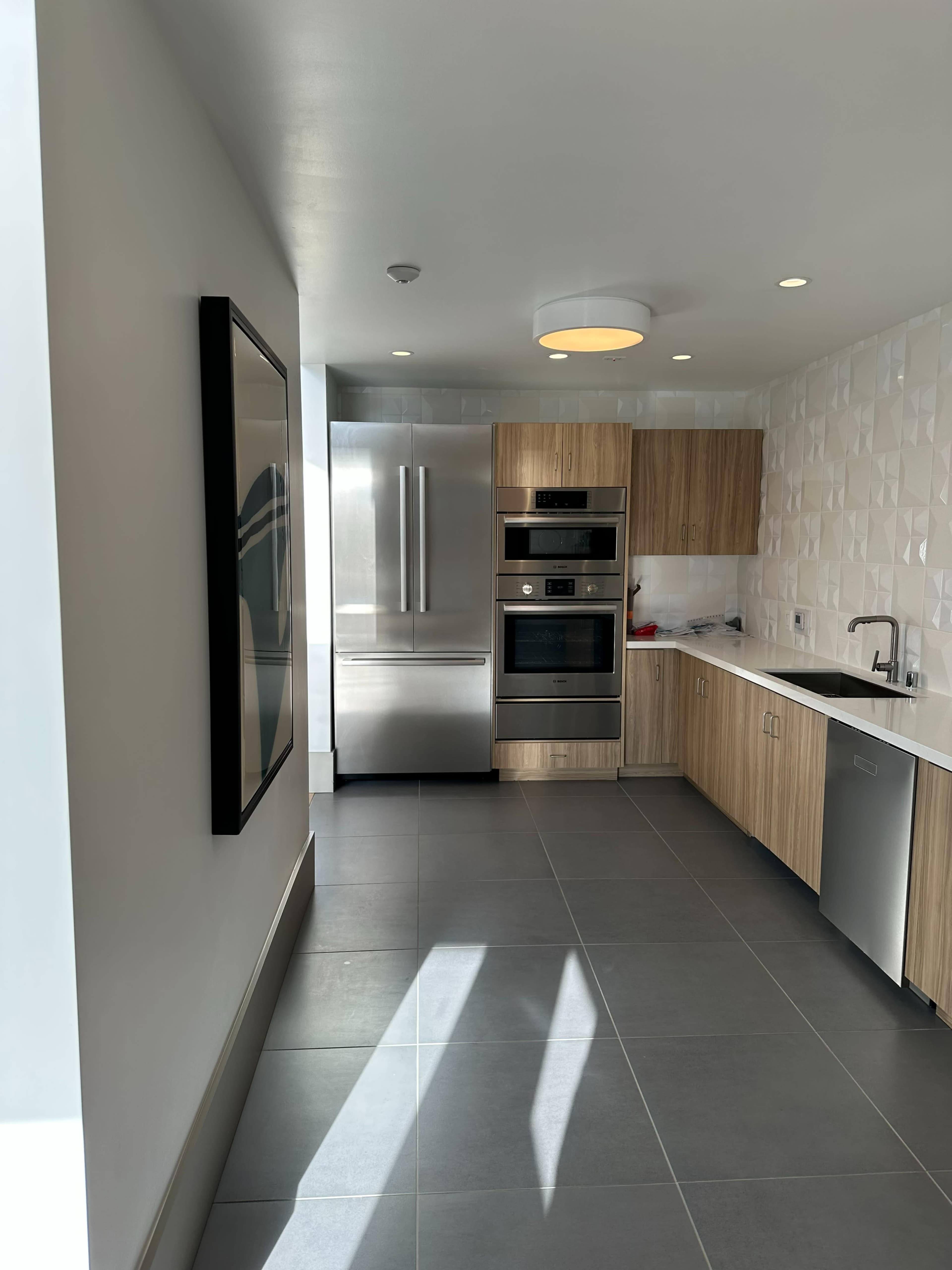 A modern kitchen with wooden cabinetry, stainless steel appliances, and gray tile flooring.