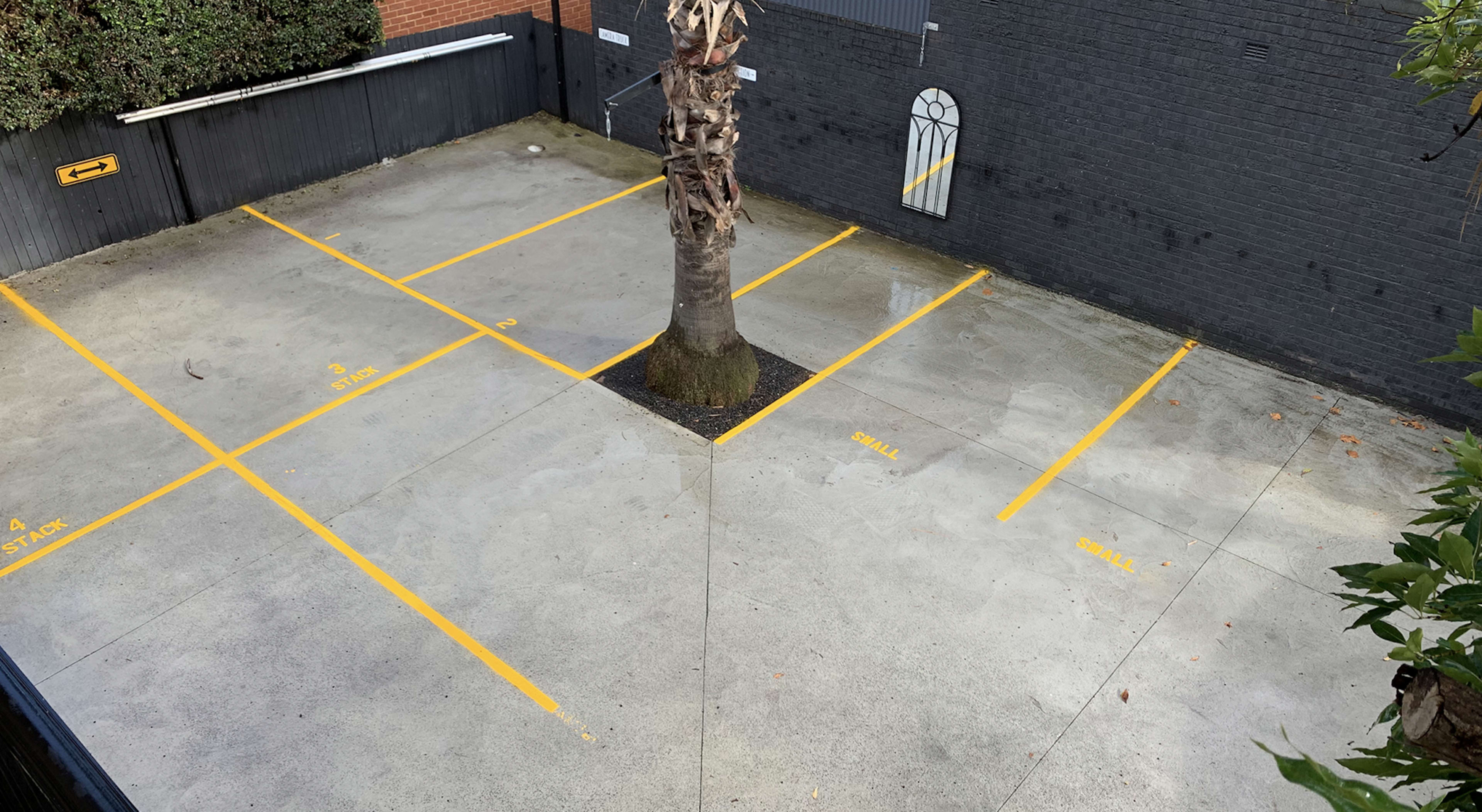 An empty parking lot features several marked spaces with a tree in the center.