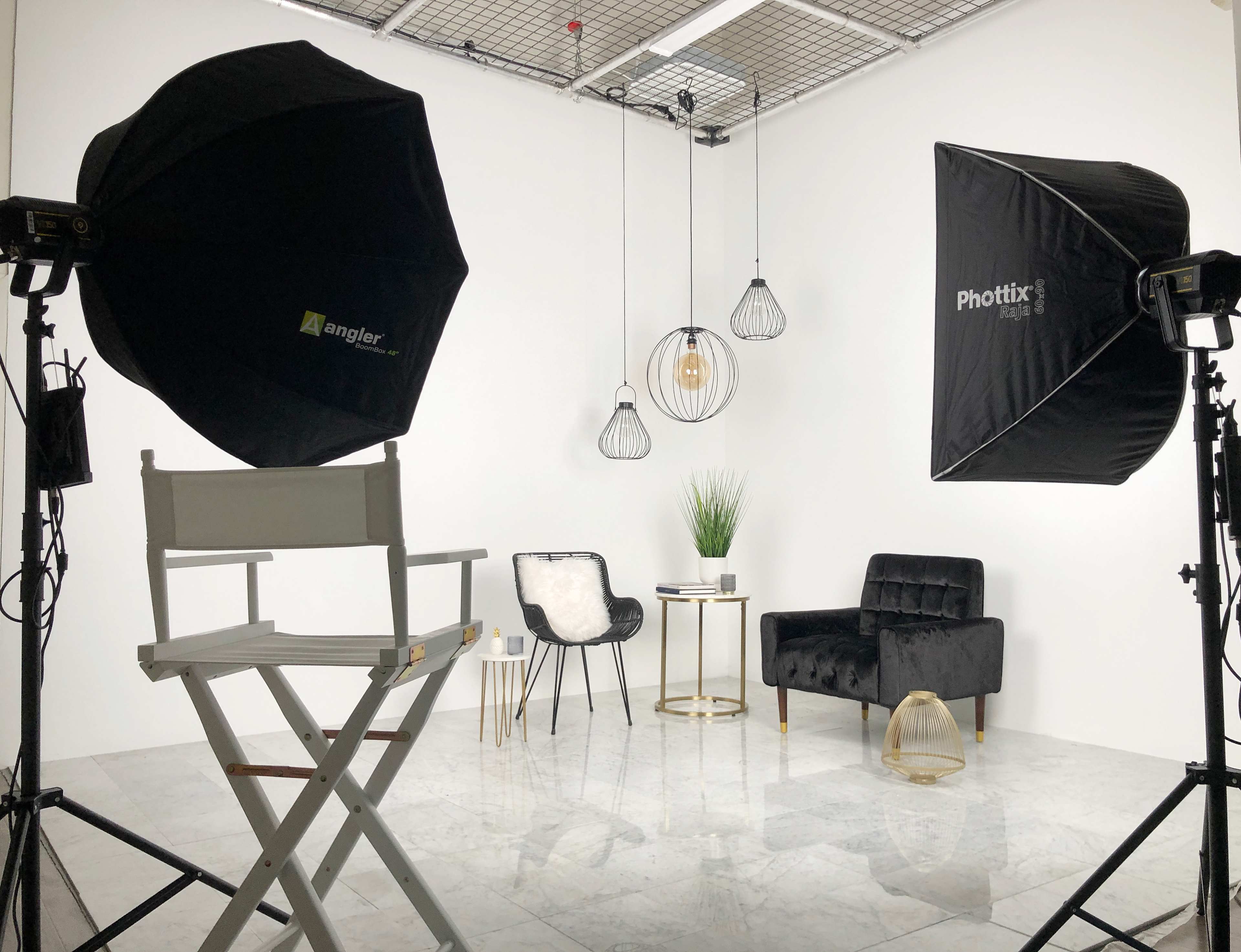 A photography studio setup with two light umbrellas, a director's chair, a small table, and a couch, all against a white backdrop.