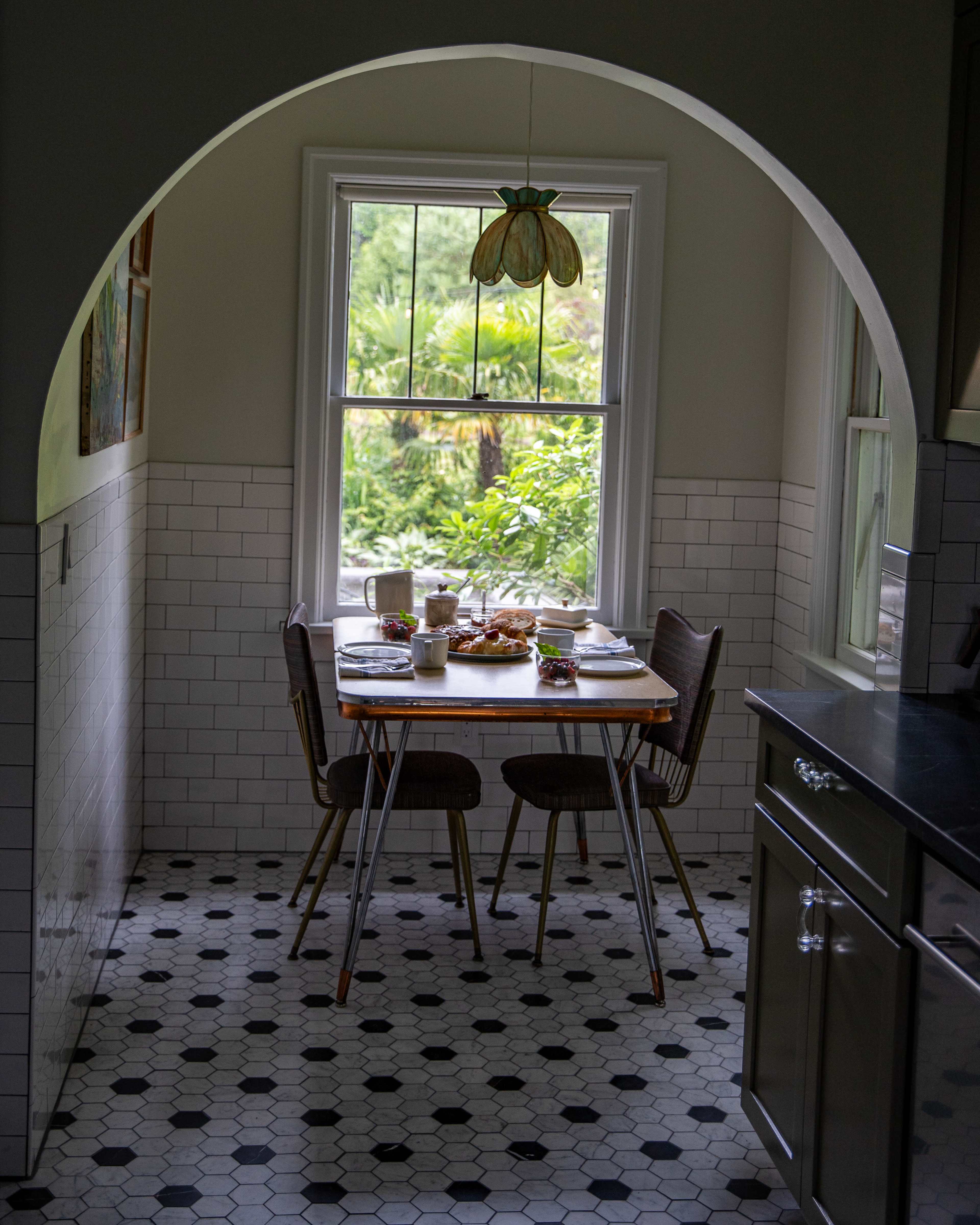A small kitchen nook features a table set for breakfast with a view of greenery through a window.