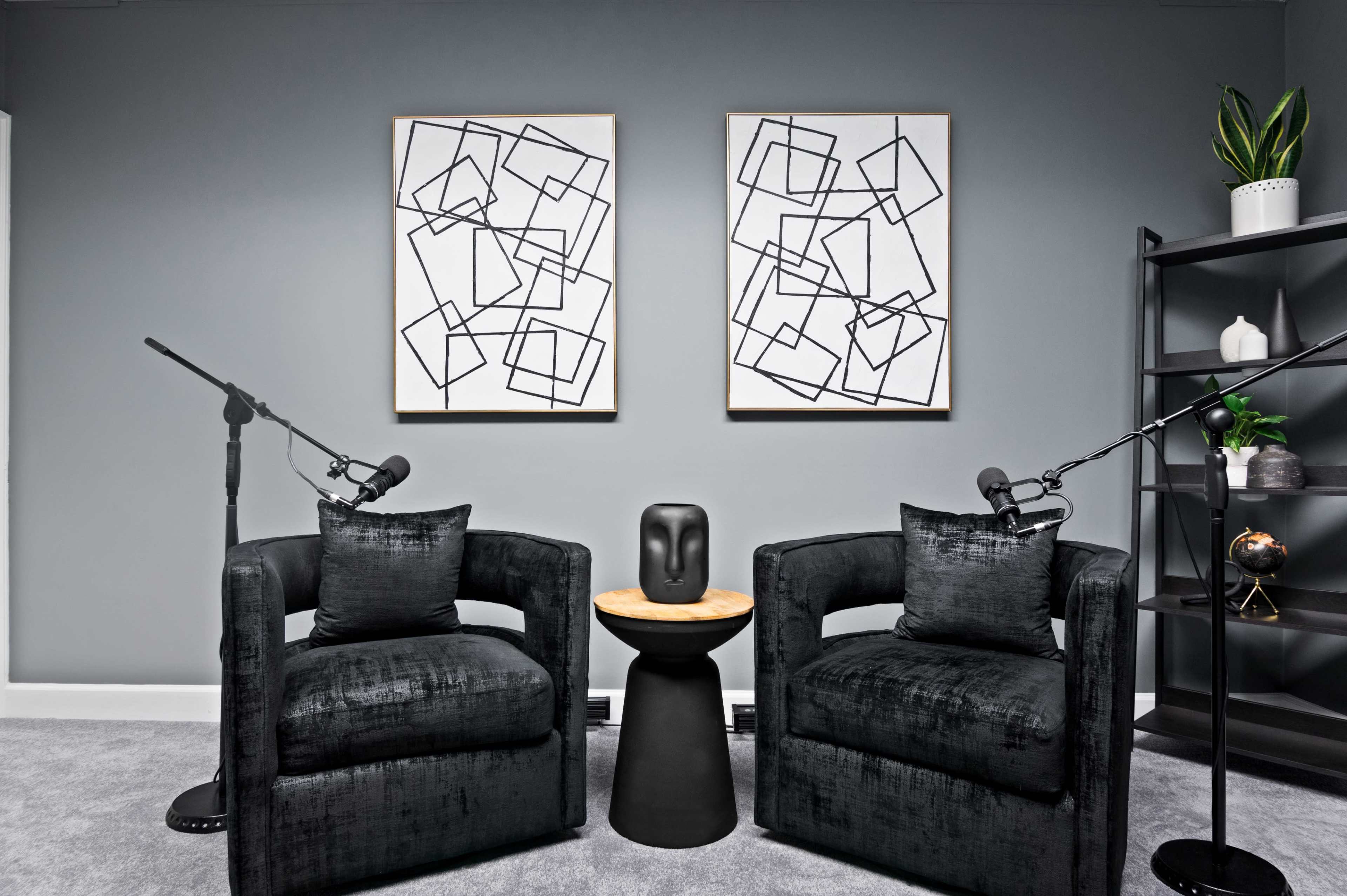 A modern sitting area features two black armchairs with microphones on stands, a small black table, and two abstract framed artworks on the wall.