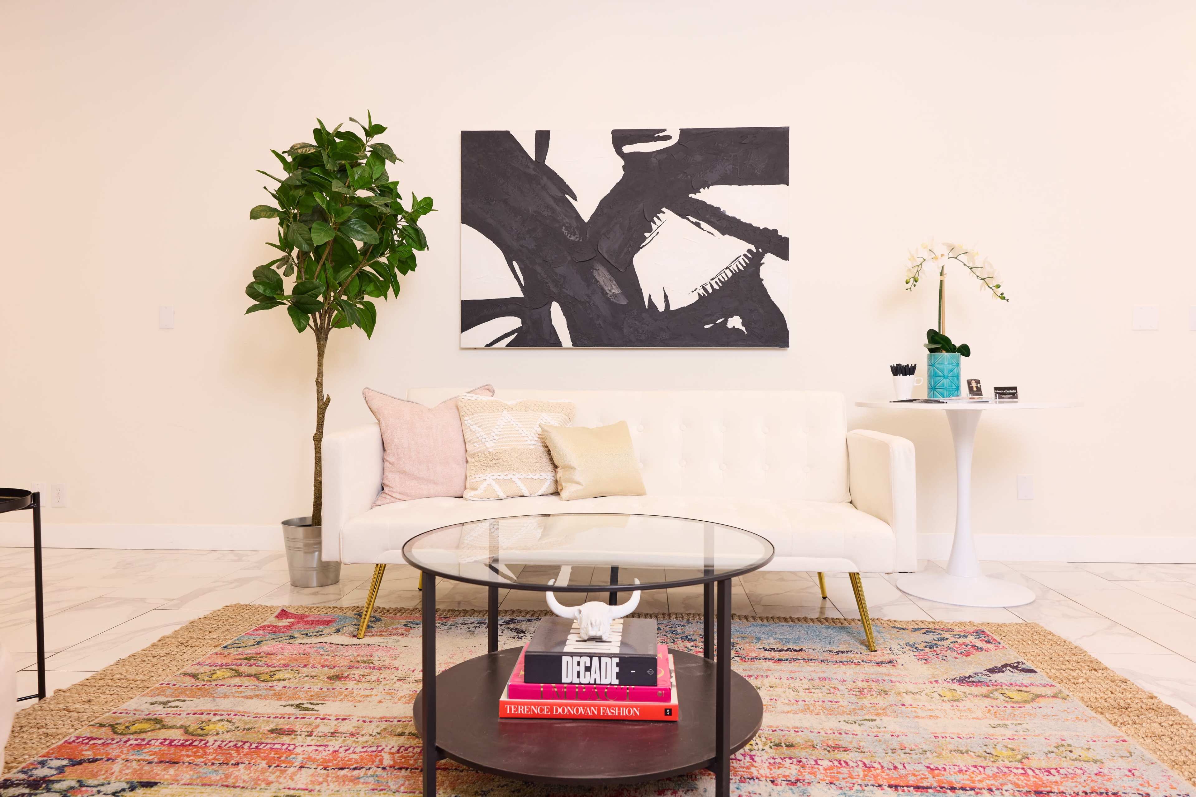 A modern living room with a white sofa, a circular glass coffee table, and a colorful patterned rug.