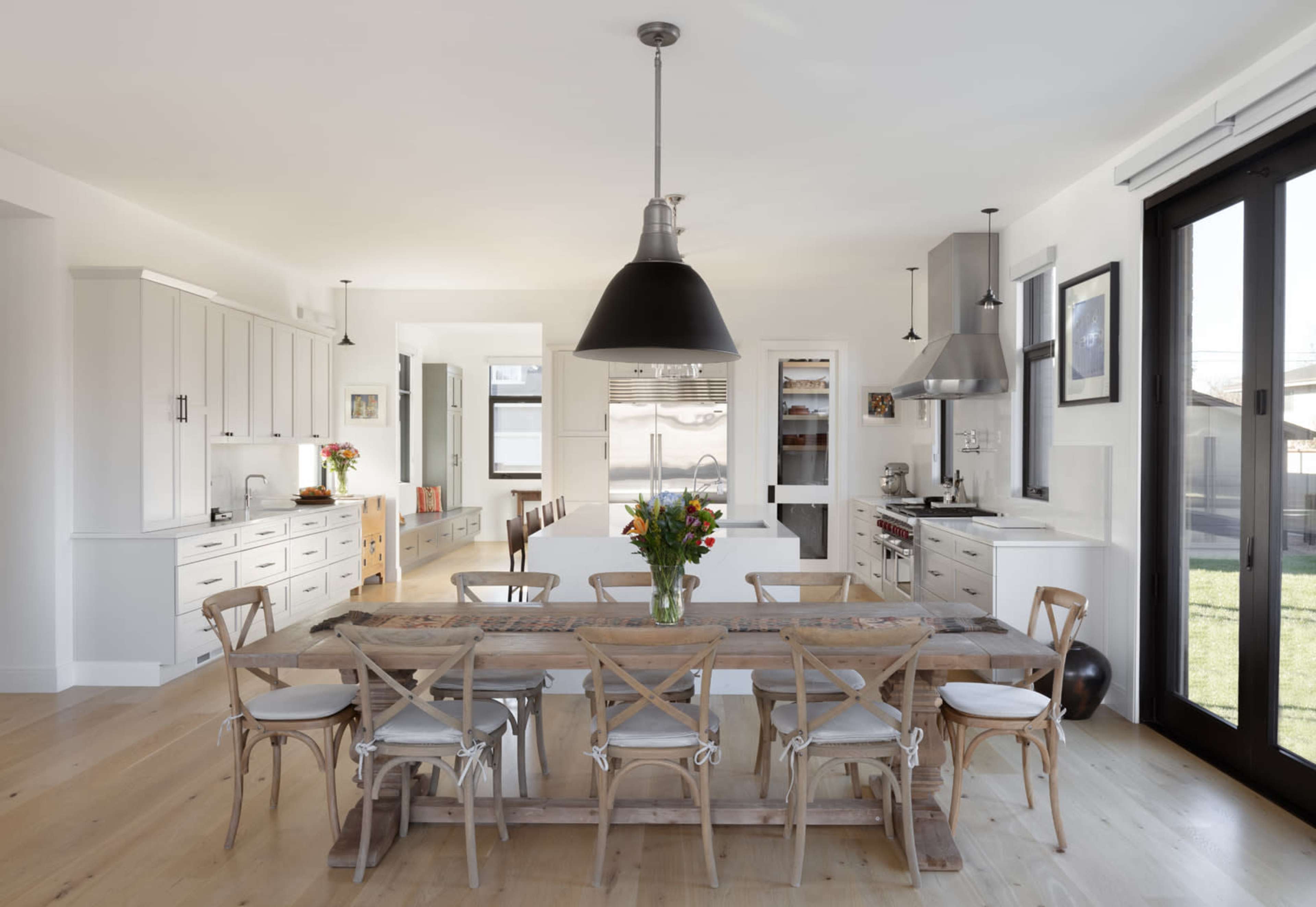 A spacious kitchen features a large wooden dining table surrounded by chairs, with modern appliances and a bright, airy layout.