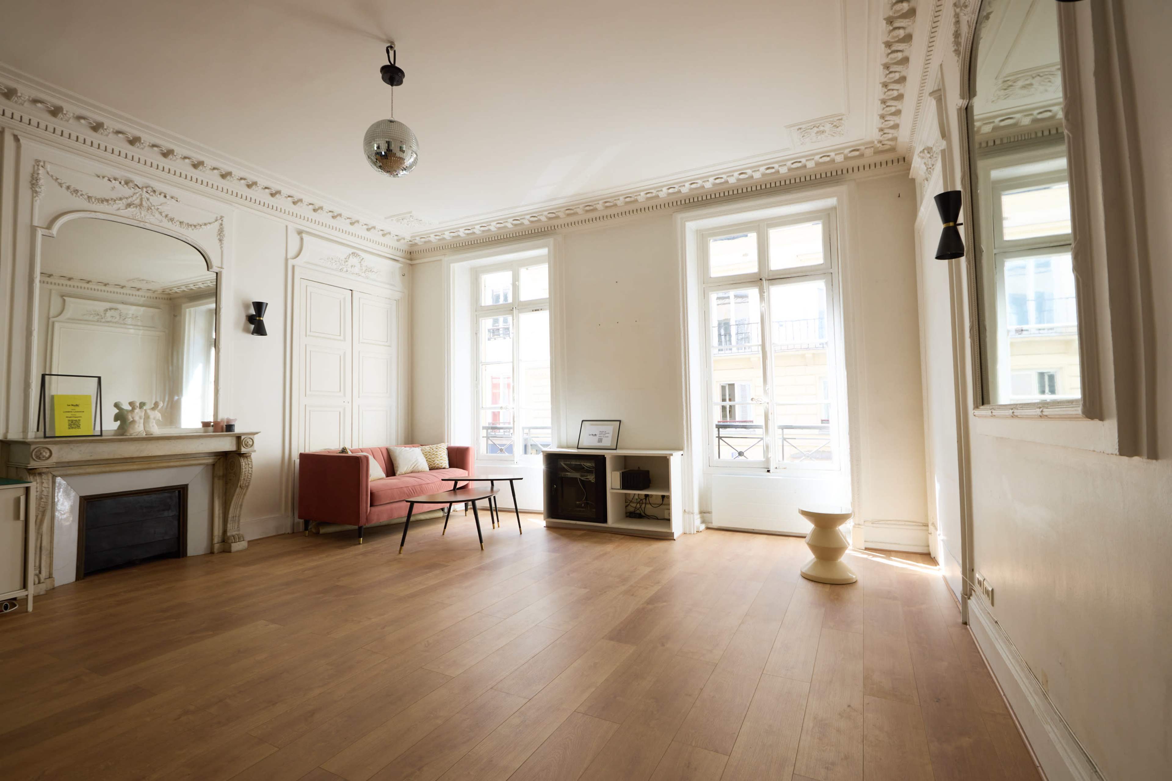 The image shows a spacious, elegantly designed living room with large windows, a pink sofa, and minimalist decor.