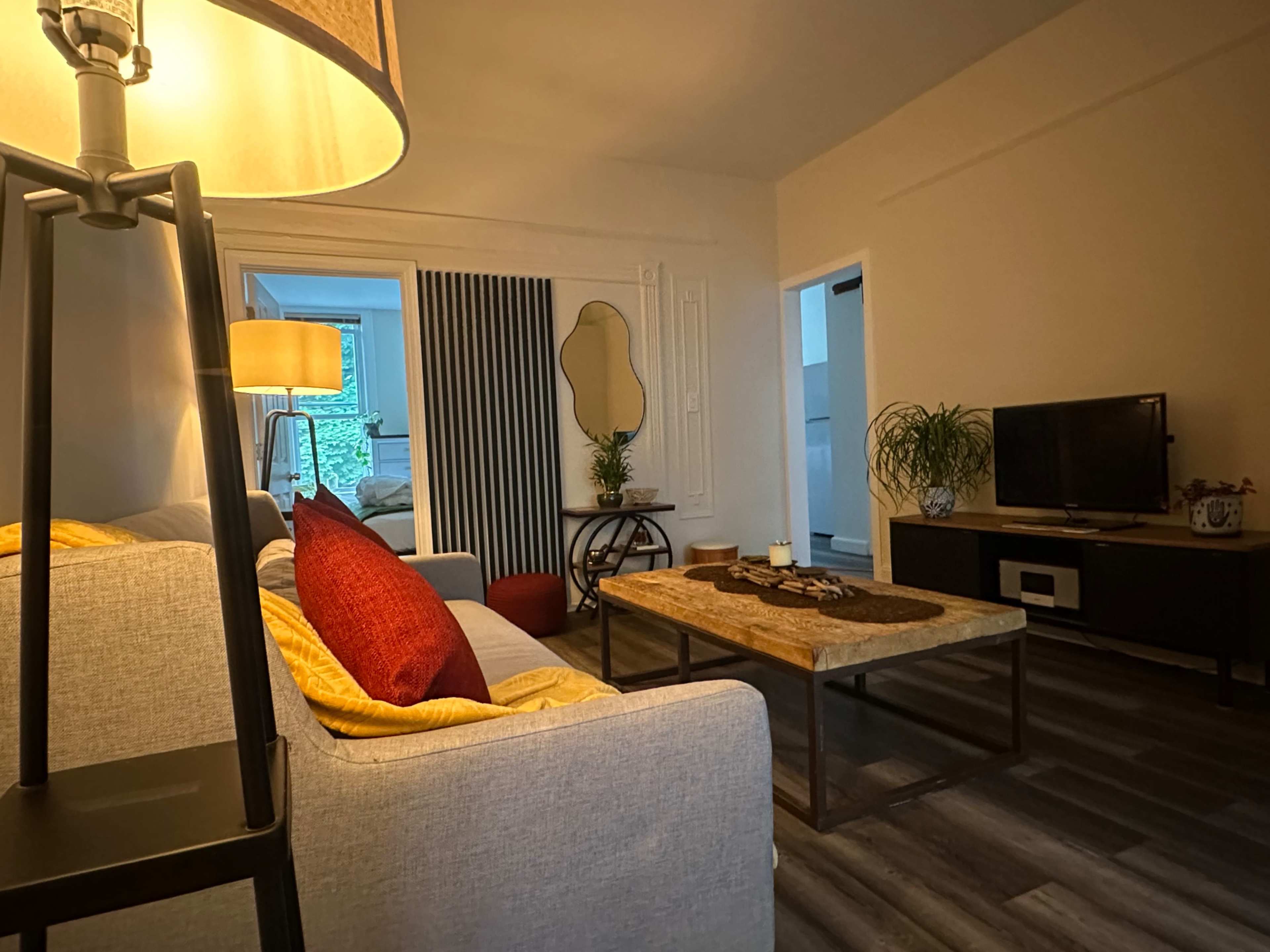 A cozy living room features a grey sofa with a red pillow, a wooden coffee table, and a television against a light-colored wall.