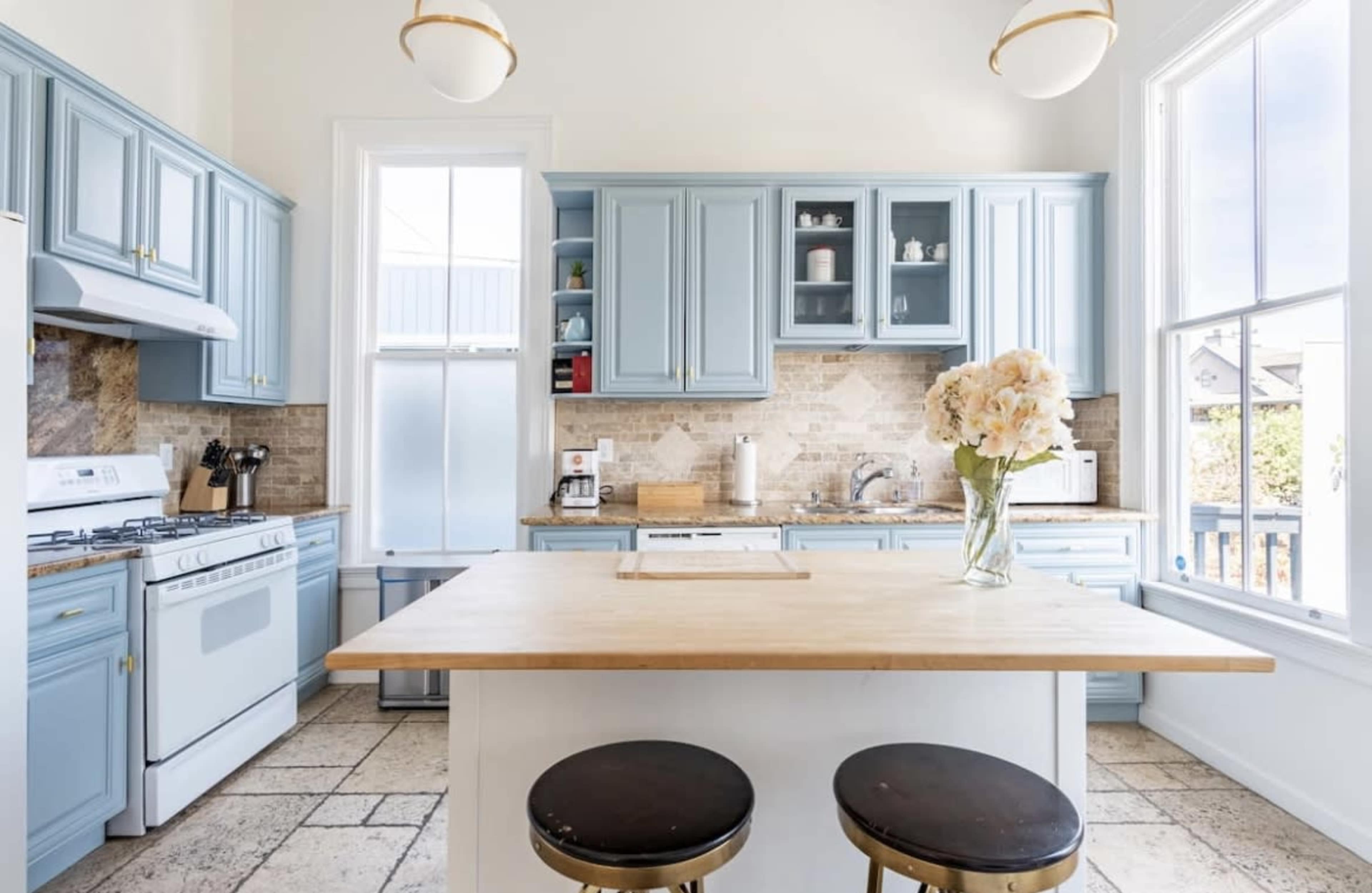 The kitchen features light blue cabinetry, a central wooden island, and a large window providing natural light.