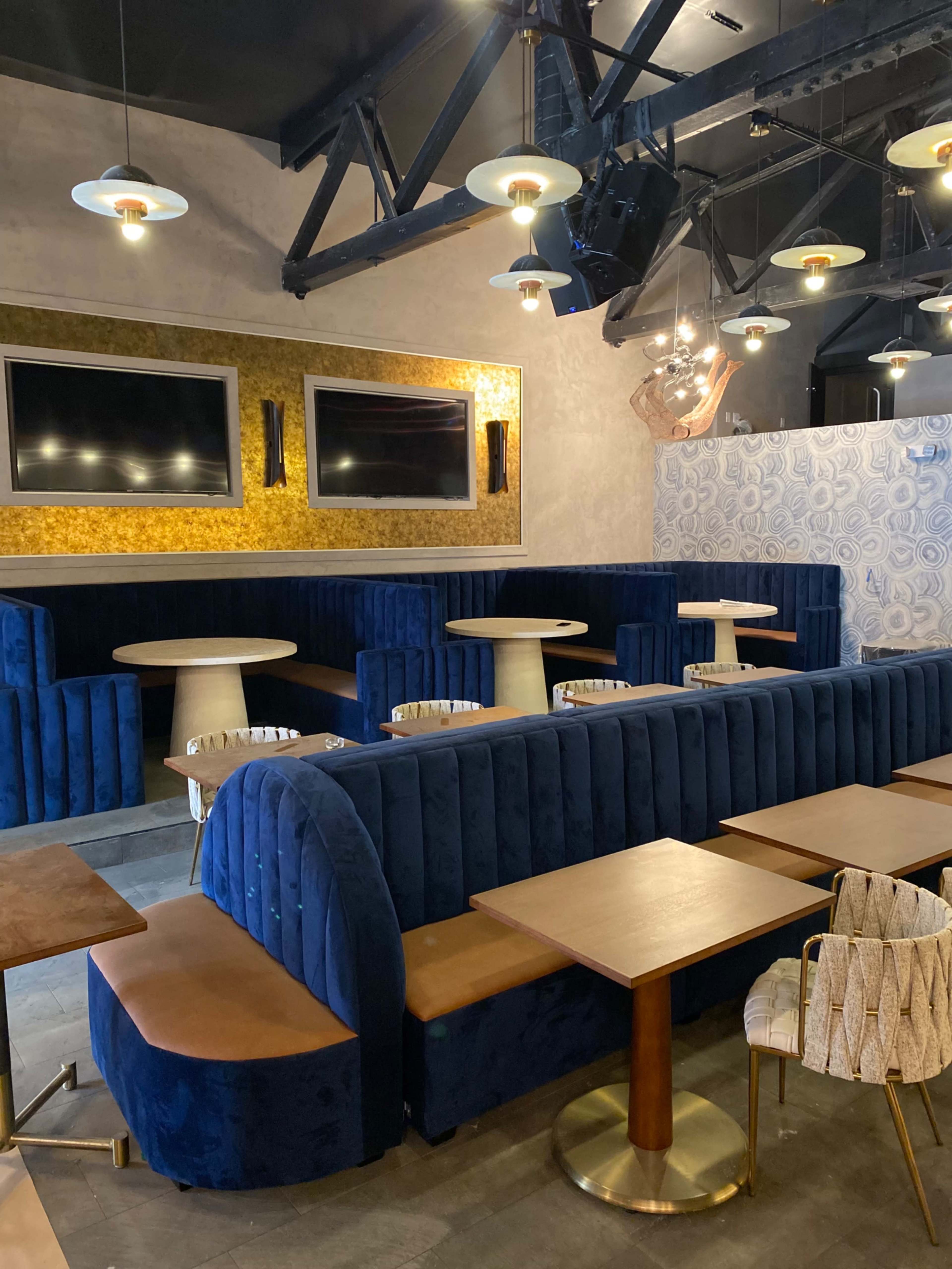 A modern interior of a café or lounge, featuring blue velvet seating, wooden tables, and decorative walls.
