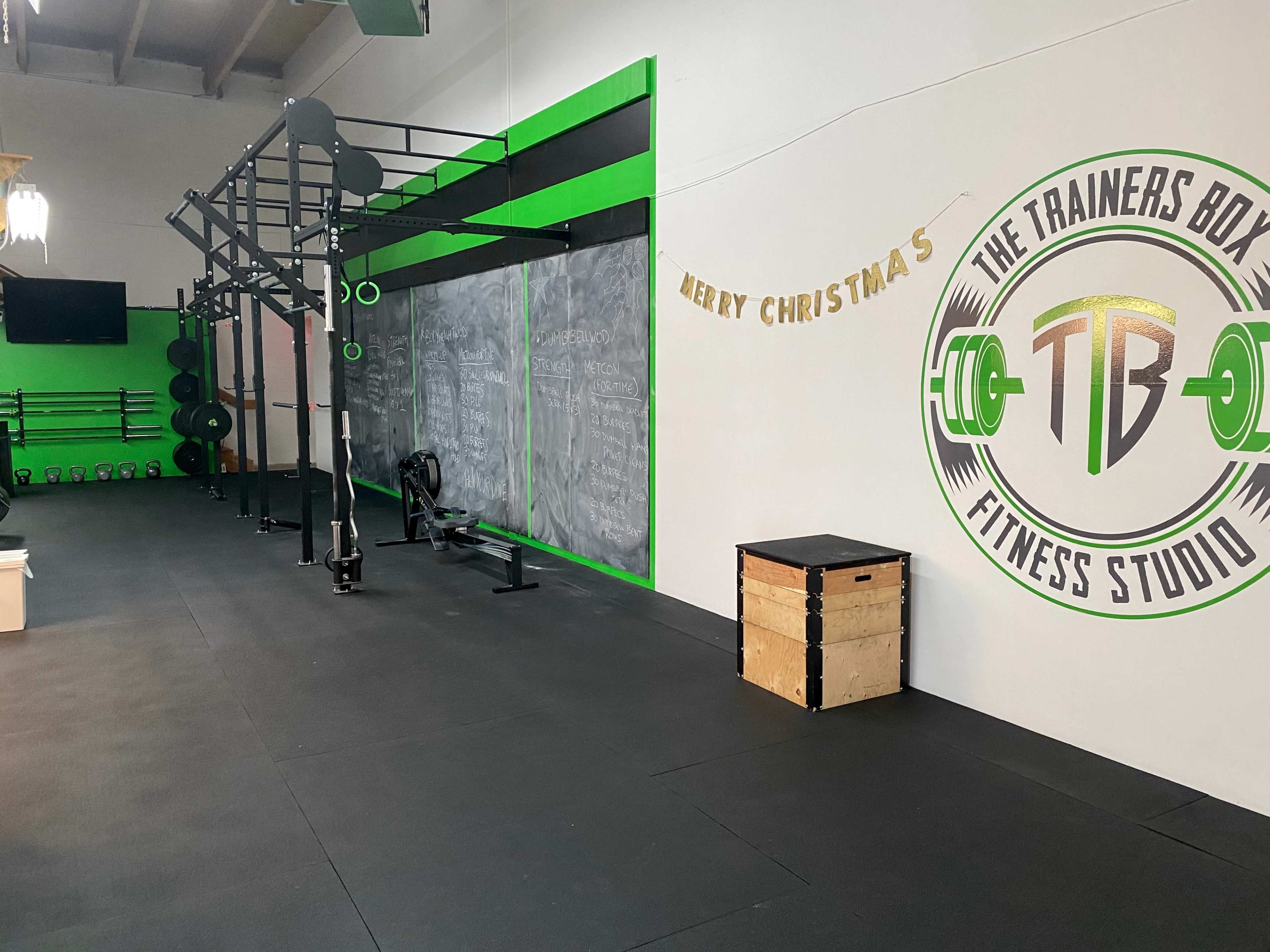 A fitness studio features a workout area with equipment like a rowing machine and dumbbells, alongside a decorated wall that says "Merry Christmas."