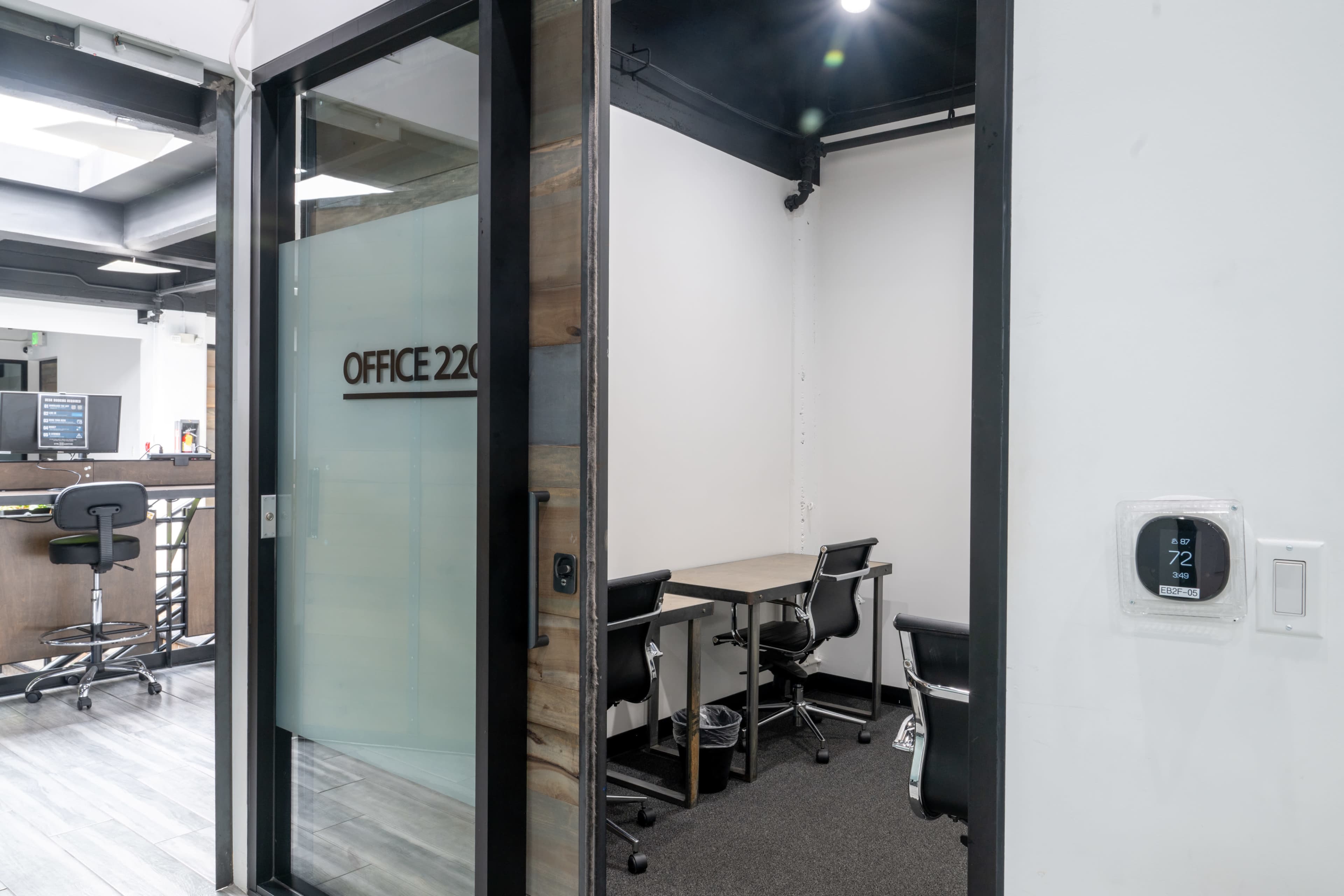 The image shows a view of an office space labeled "OFFICE 220," featuring a table and chairs inside, with a visible thermostat on the wall outside the office.
