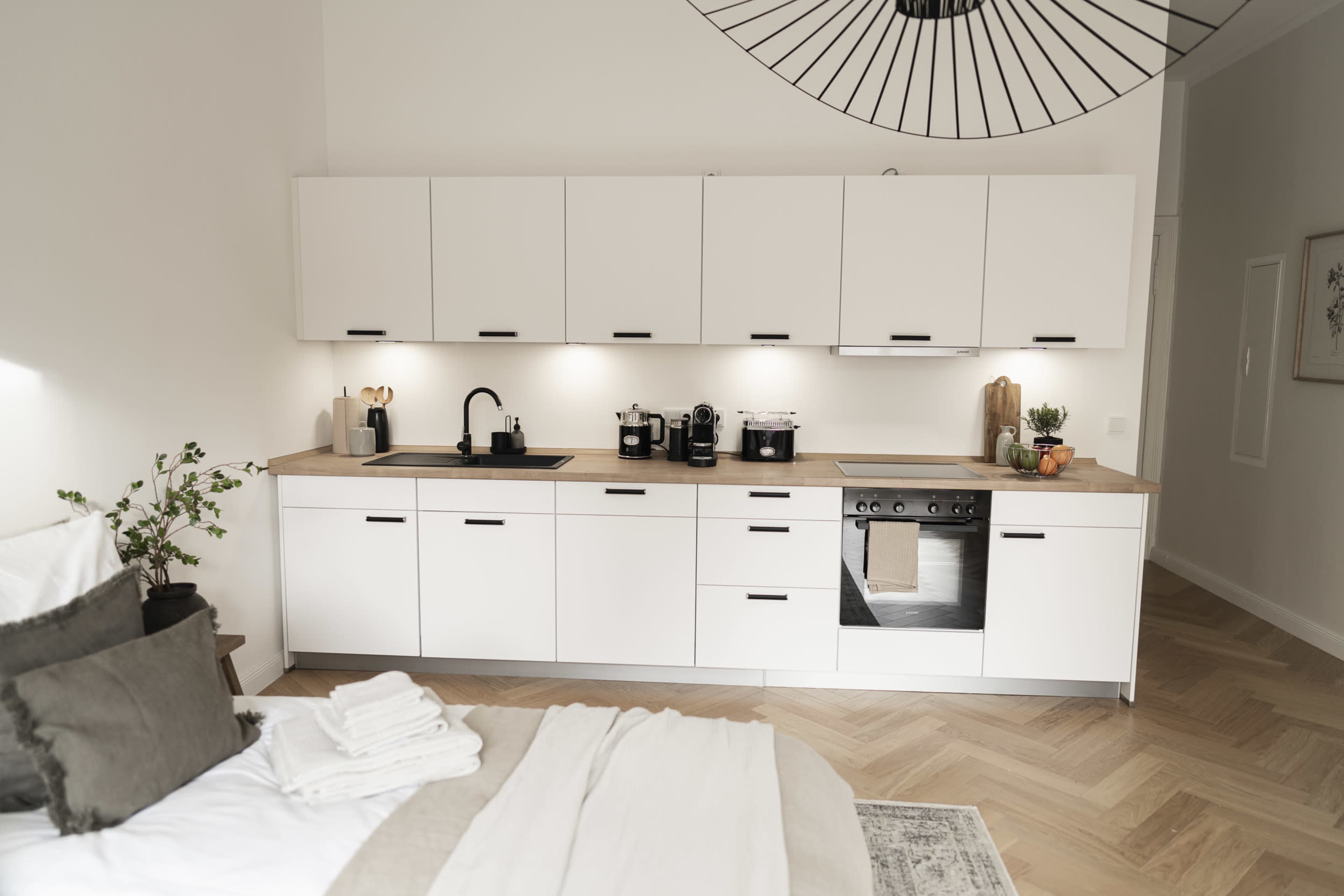 The image shows a modern kitchen with white cabinets, a wooden countertop, and a variety of kitchen appliances arranged neatly.