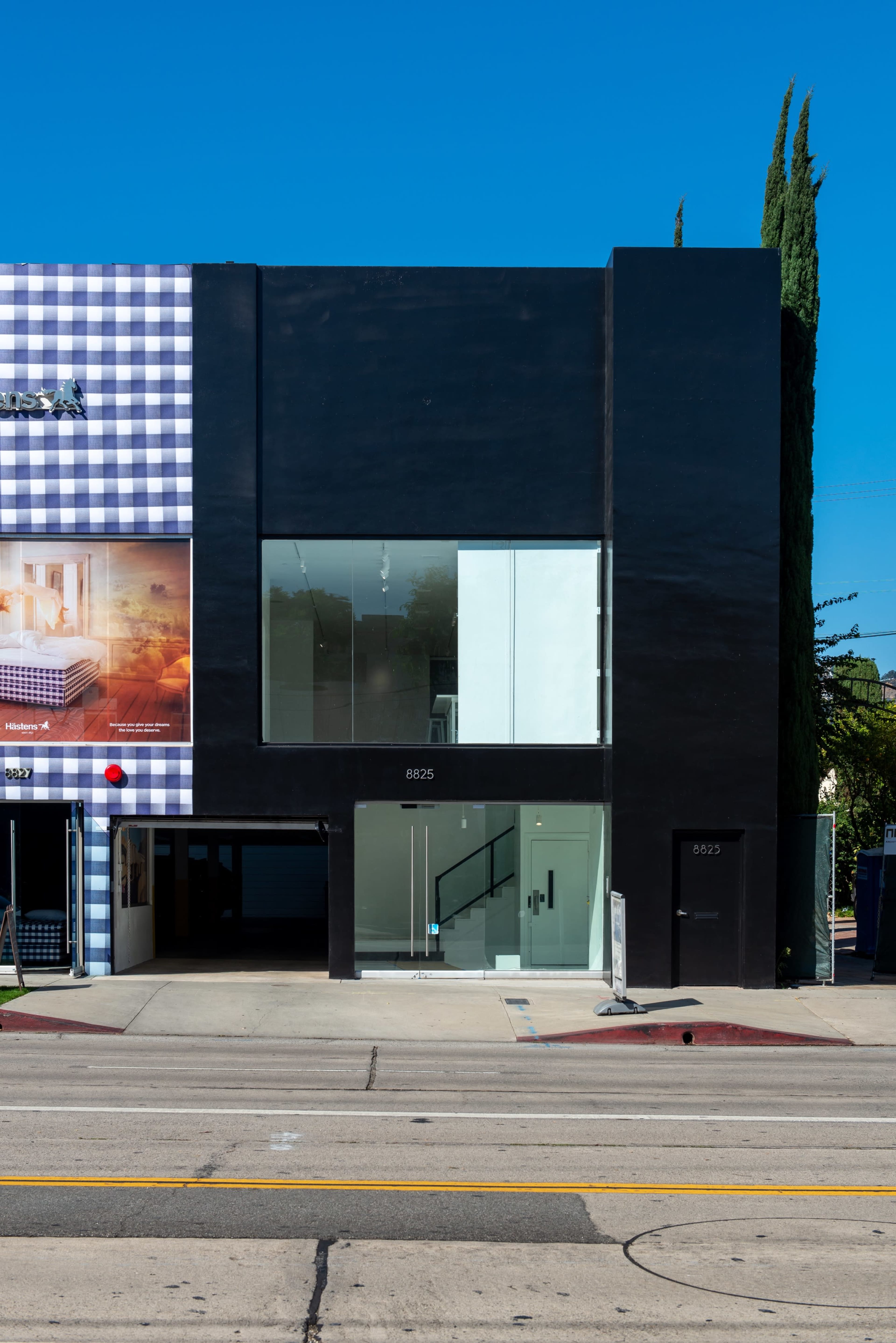 A modern black building with large glass windows and an entrance, located on a street.