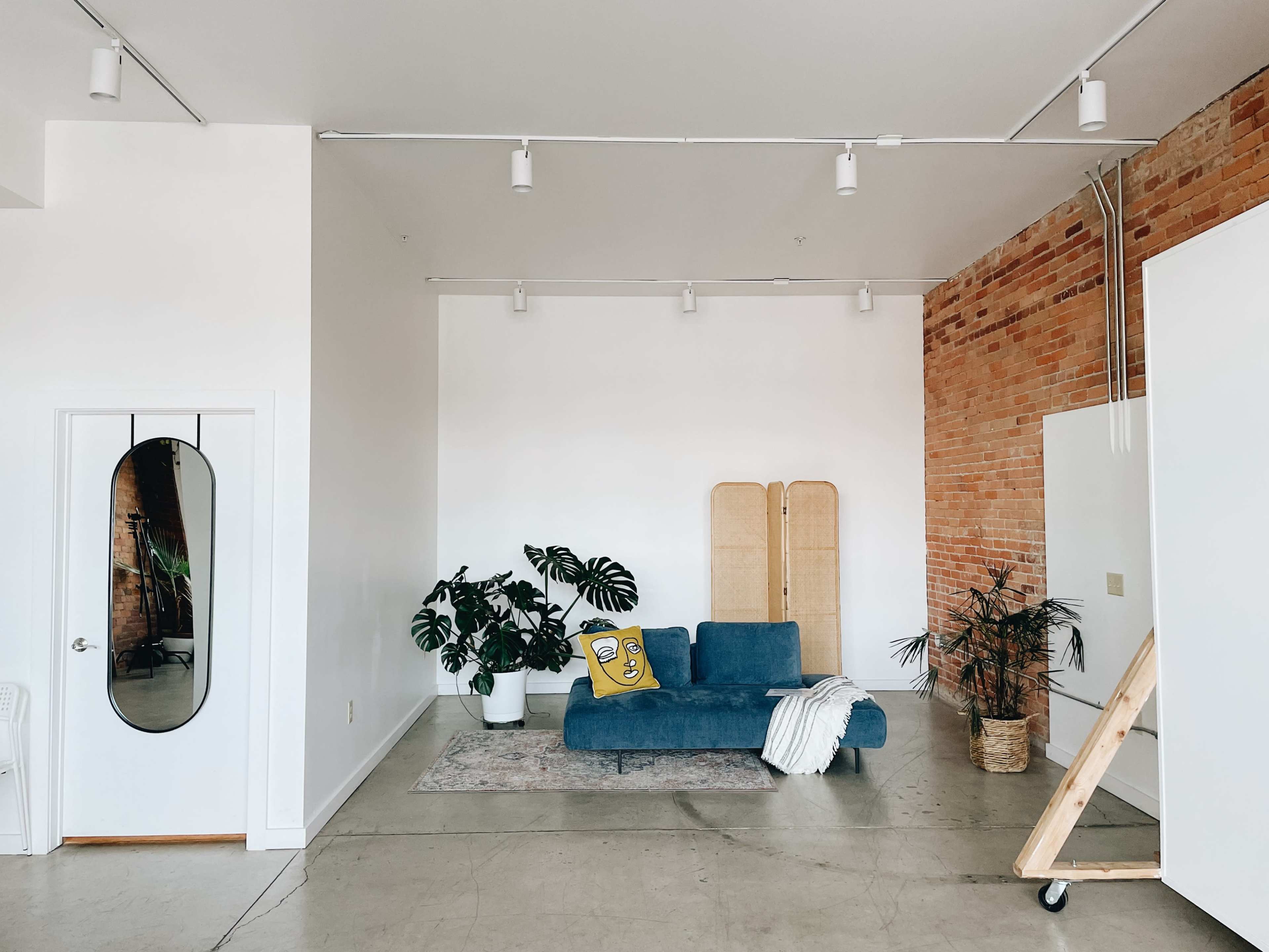 A minimalist interior features a blue couch, a large plant, and a decorative room divider against a backdrop of exposed brick walls.