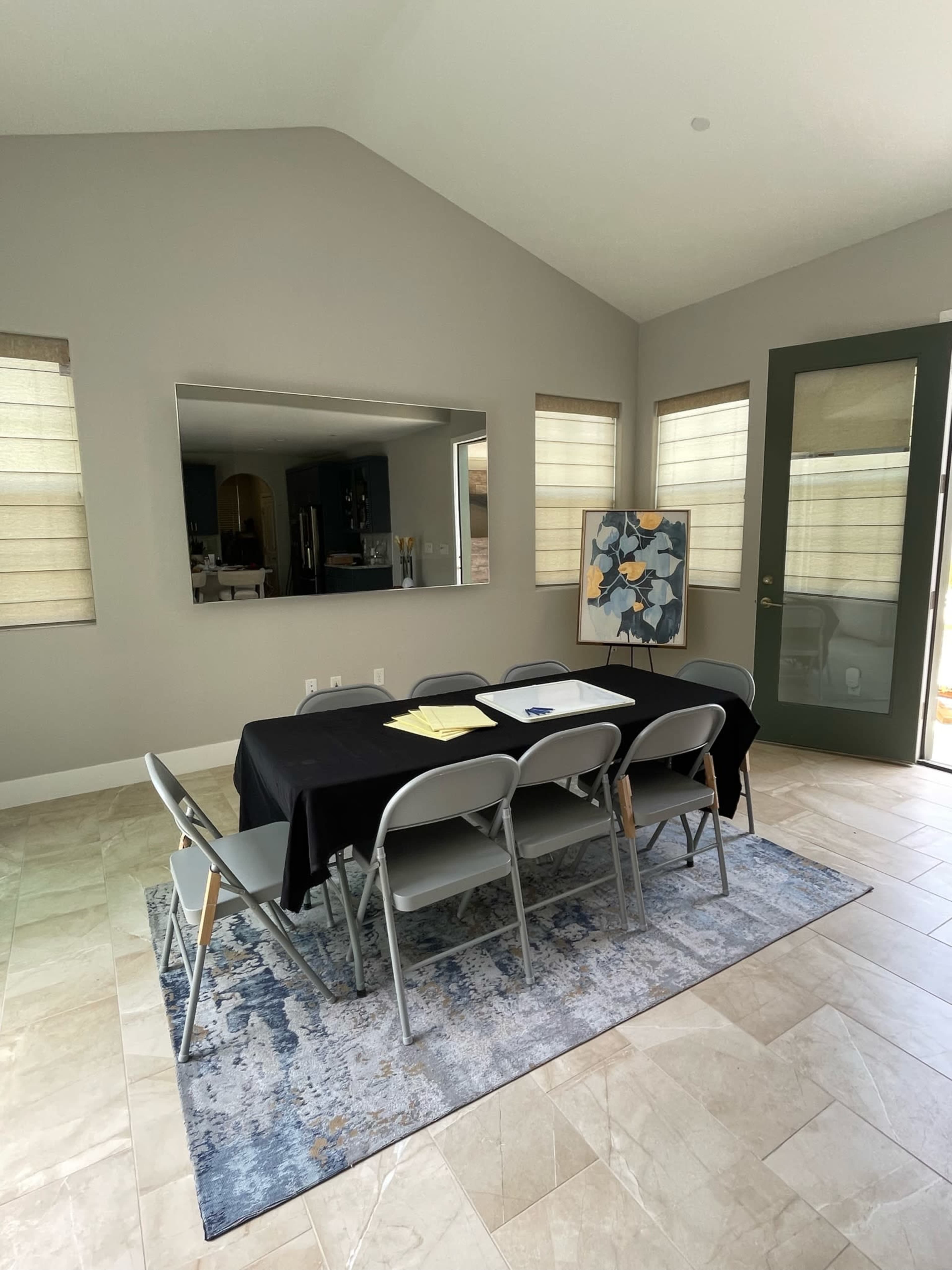 A conference room features a black table with chairs, a rug, and a large mirror on the wall, with a door leading outside.