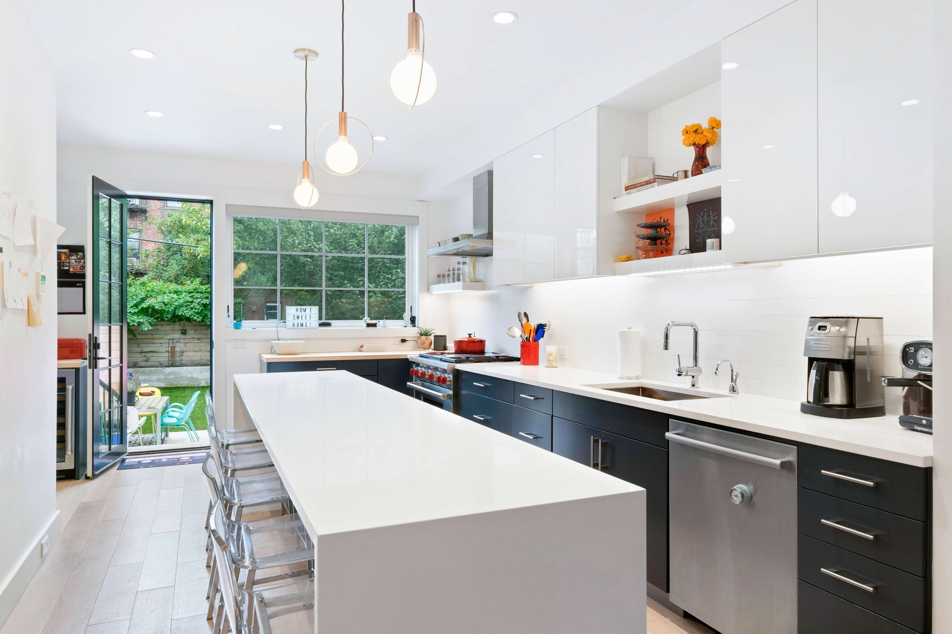 A modern kitchen features a large central island with seating, sleek cabinetry, and a window that opens to a green outdoor space.