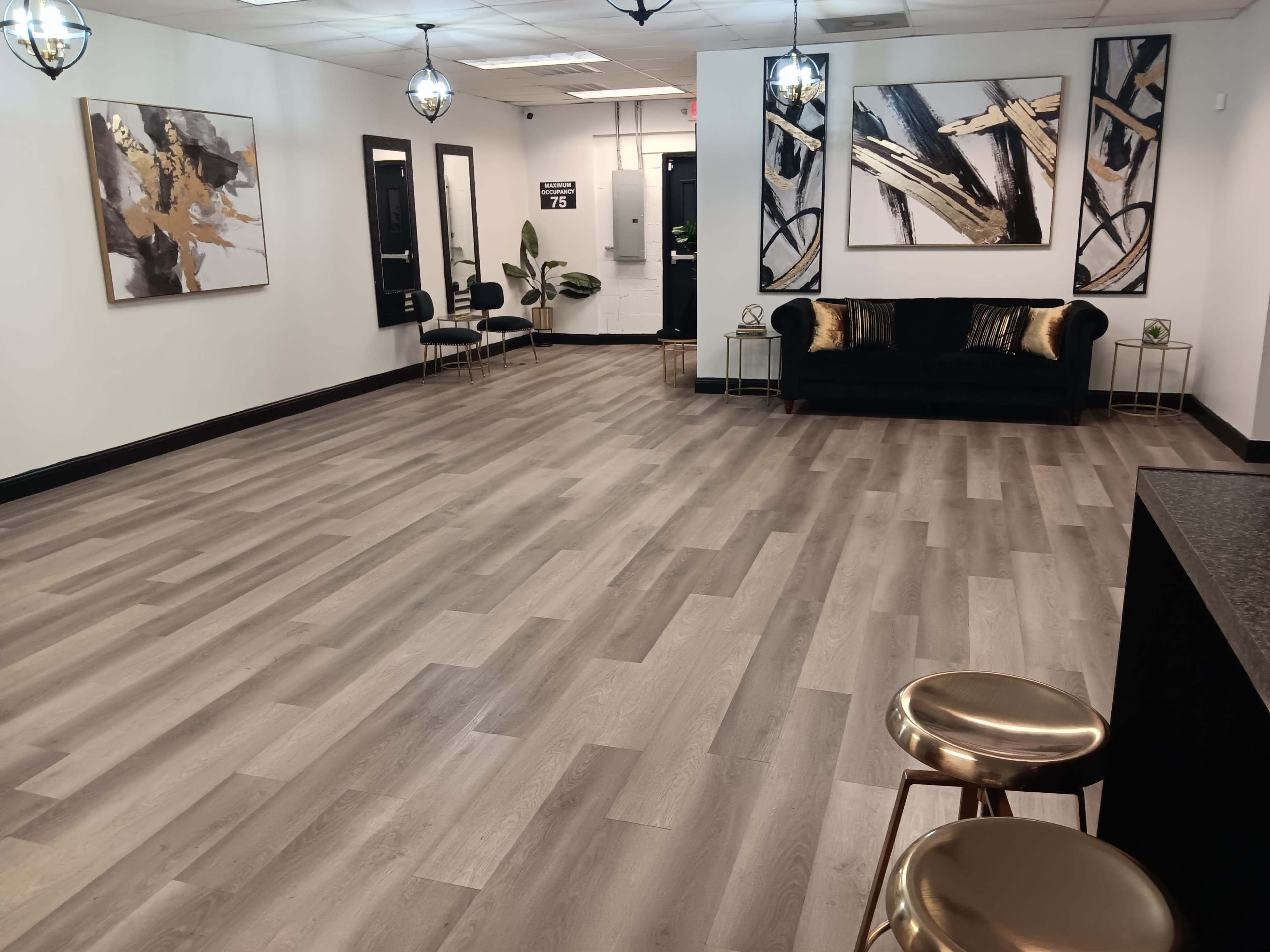 A spacious, modern interior with light wooden floors, black and gold furniture, and abstract wall art.