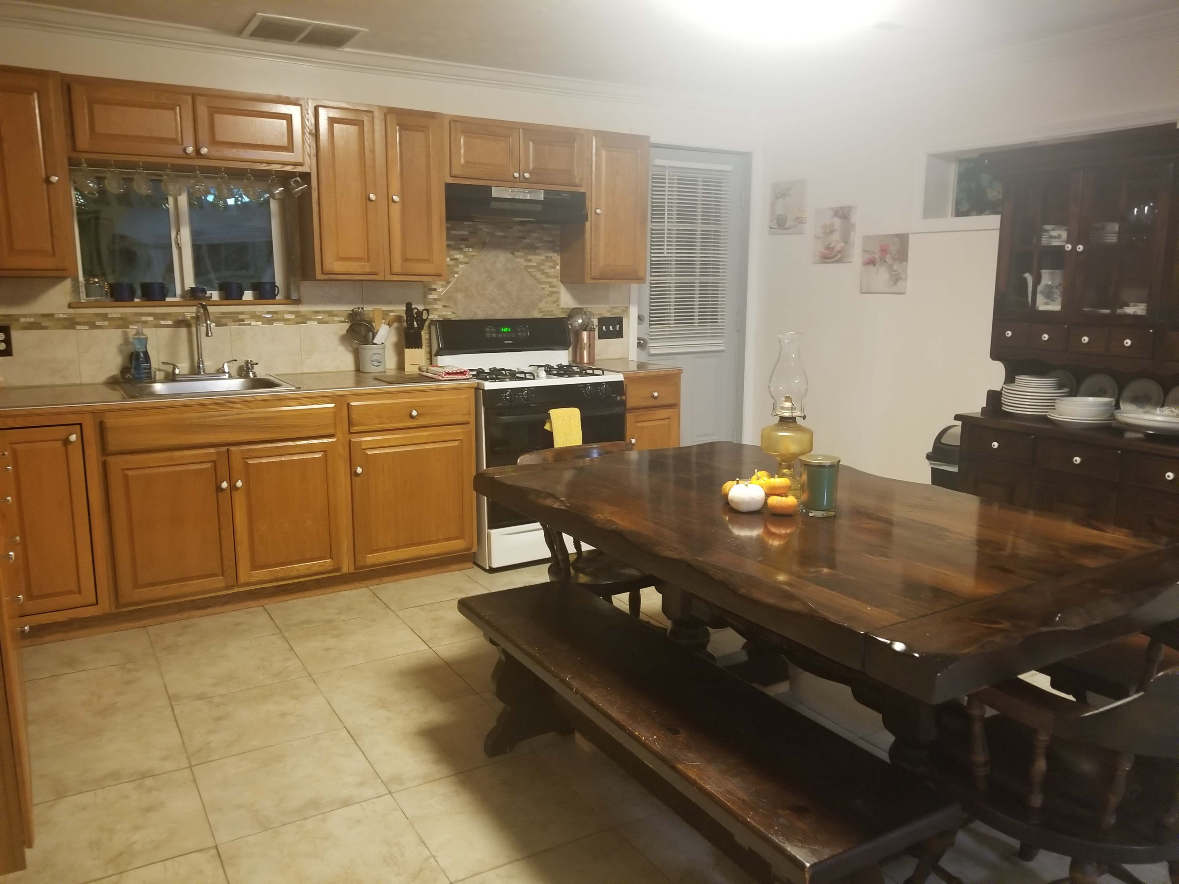 A kitchen with wooden cabinetry, a gas stove, and a large dining table set with candles and decorative items.