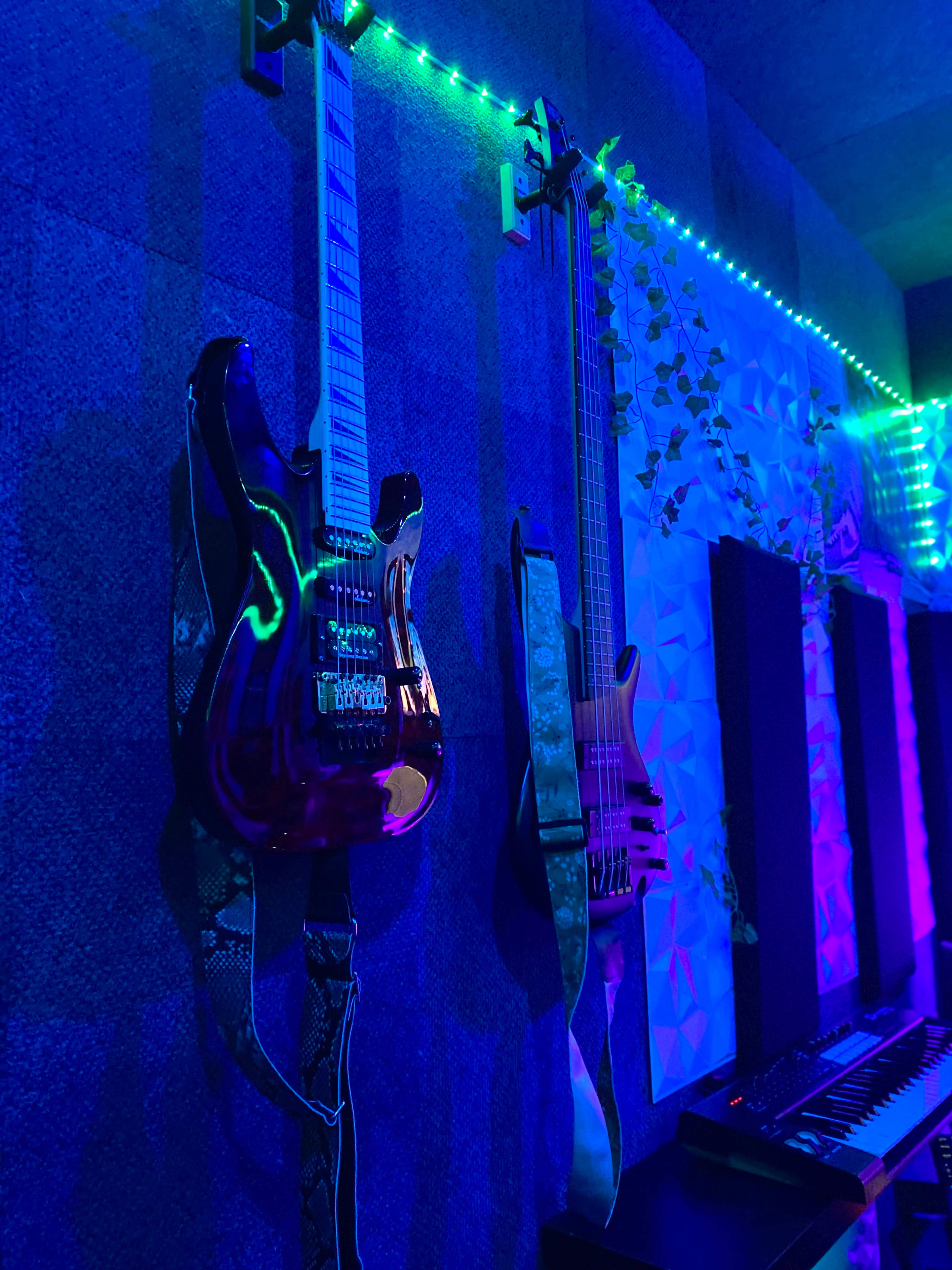 Two electric guitars are mounted on a wall with LED lights illuminating the scene in blue and green hues.