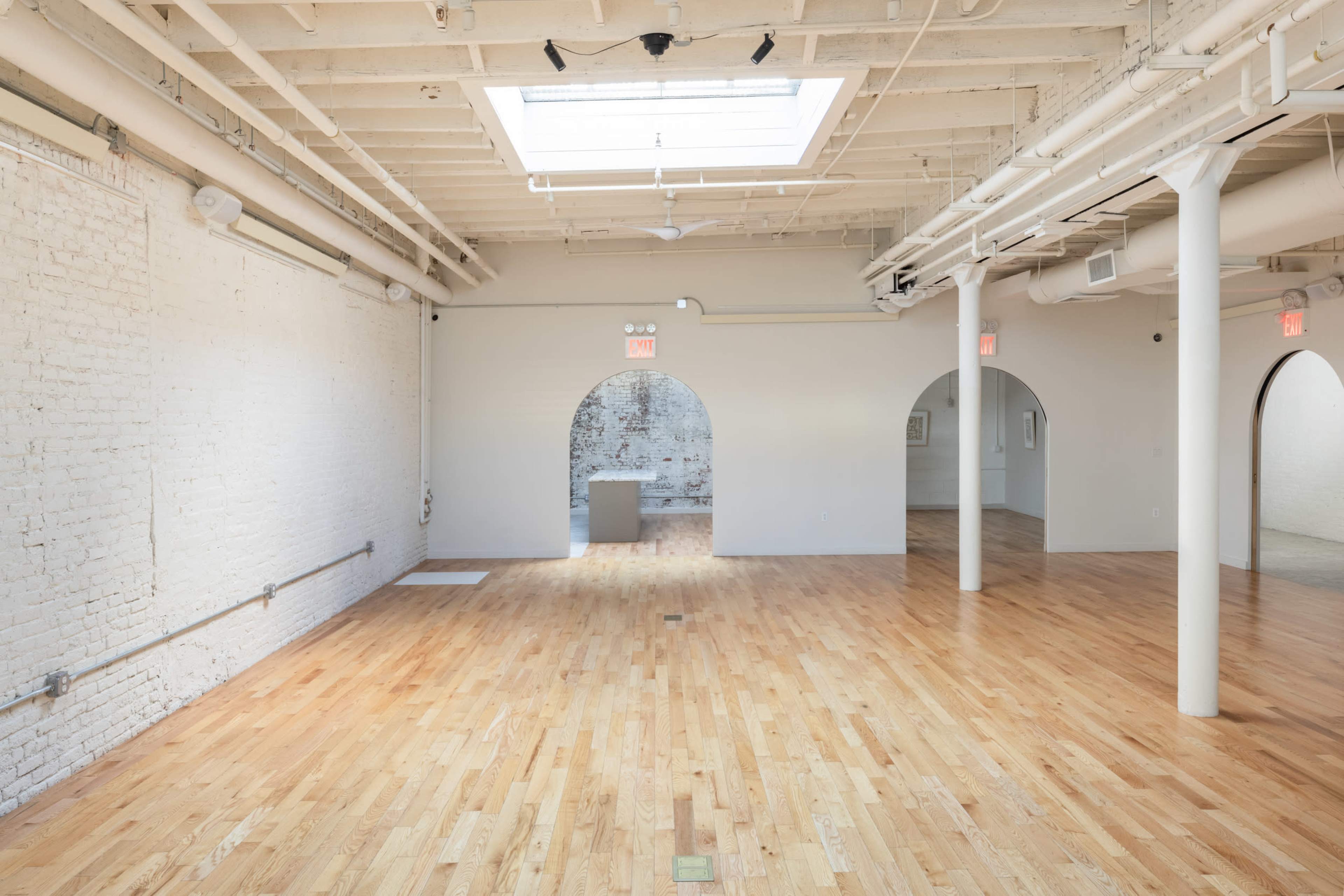 A spacious room with wooden flooring features white brick walls and multiple archways leading to other areas.