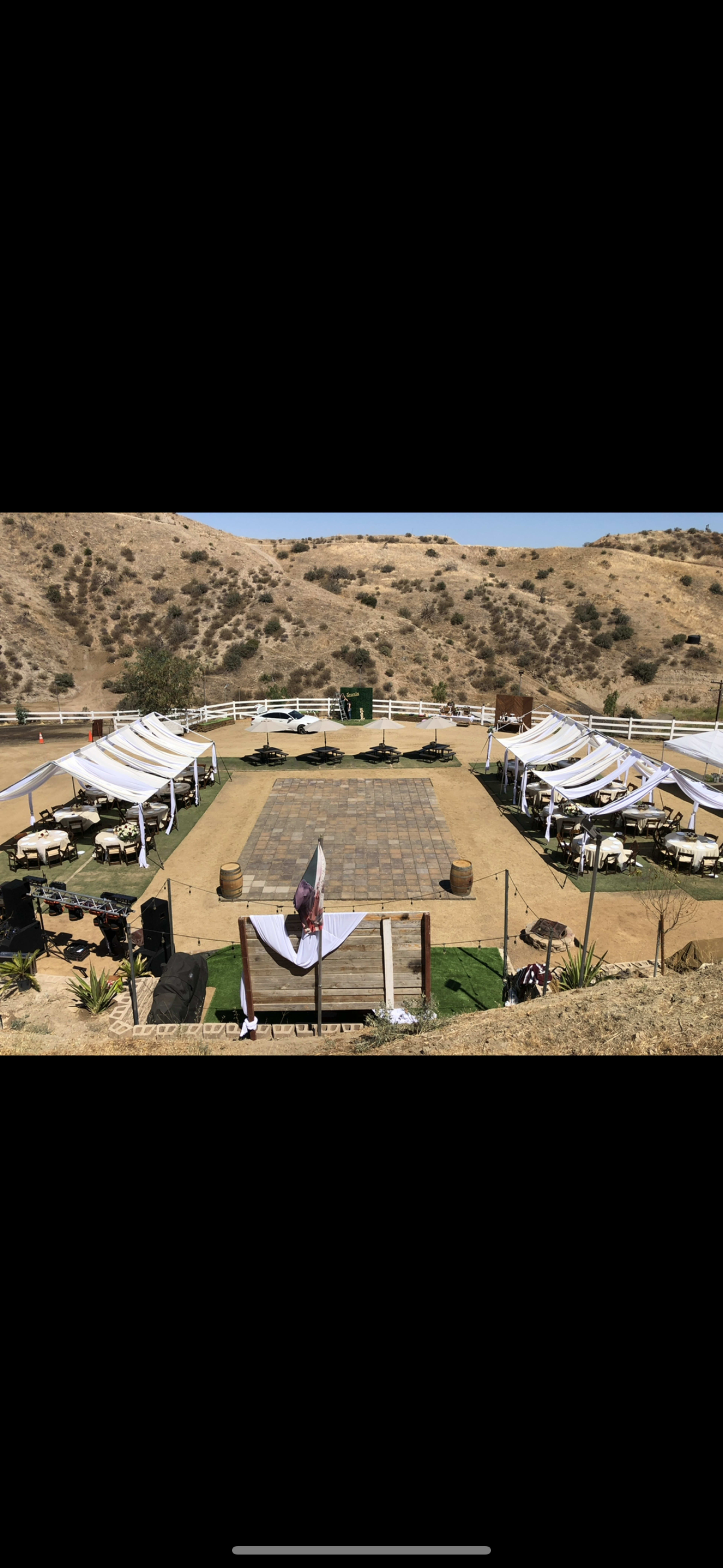 The image shows an outdoor event space set up with tables and tents arranged around a central dance floor in a hilly landscape.