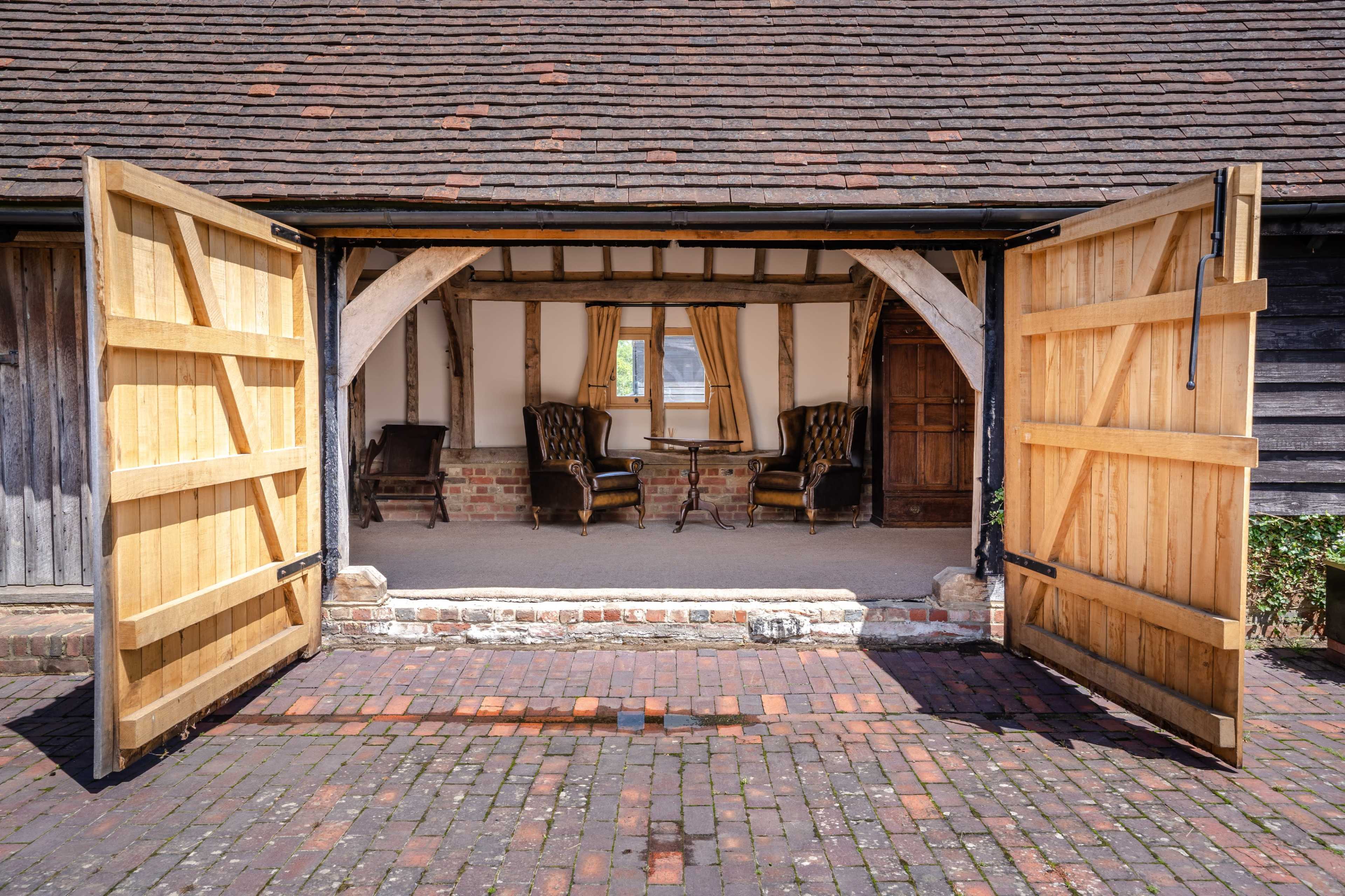 Open wooden double doors leading into a room with two chairs and a window, framed by a rustic building structure.