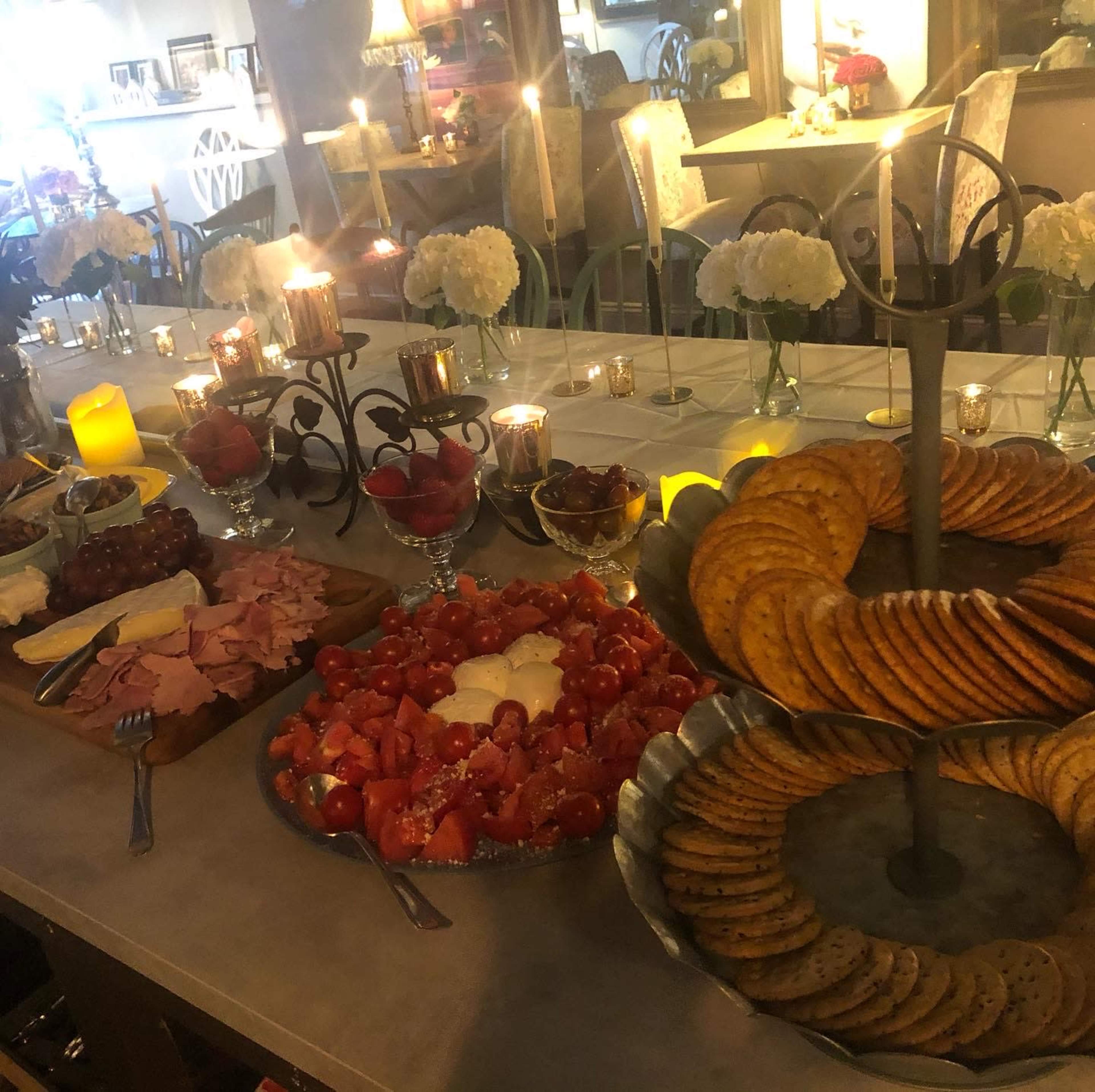 A buffet table set with various foods, including fruit, meat, cheese, and cookies, surrounded by candles and floral arrangements.