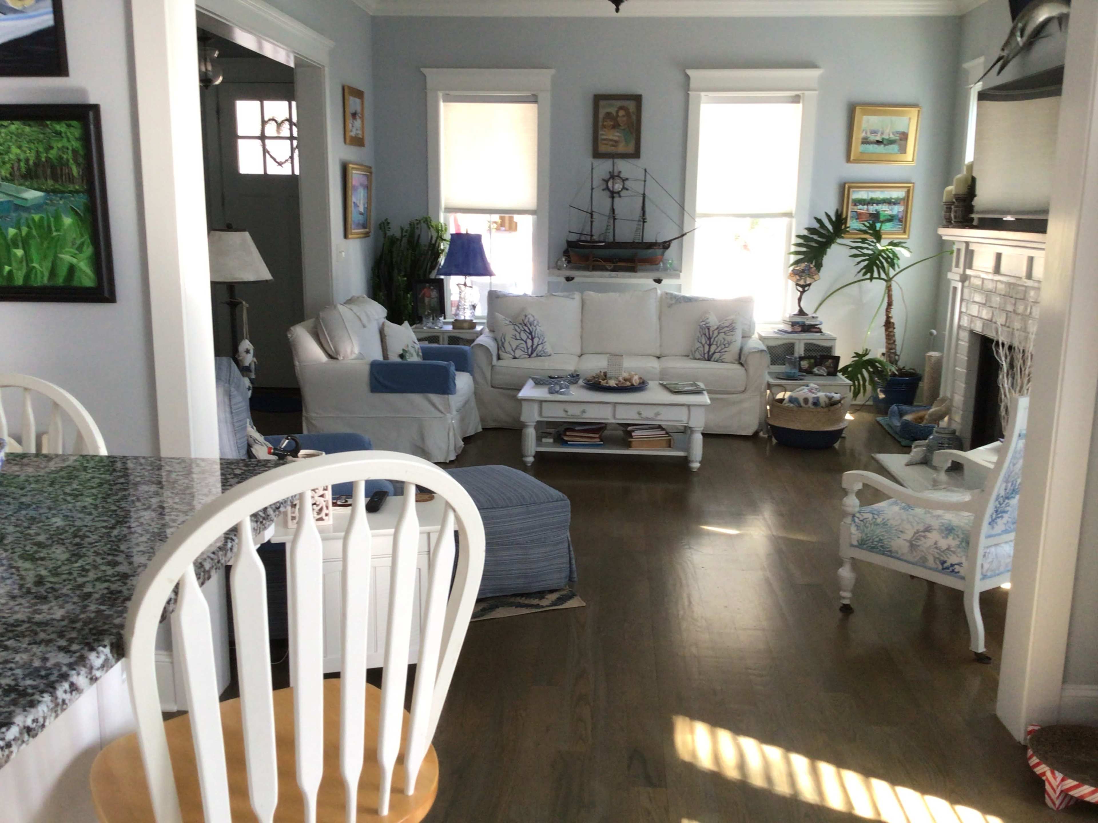 A bright living room with white furniture, light blue walls, and a decorative sailboat on the mantel.