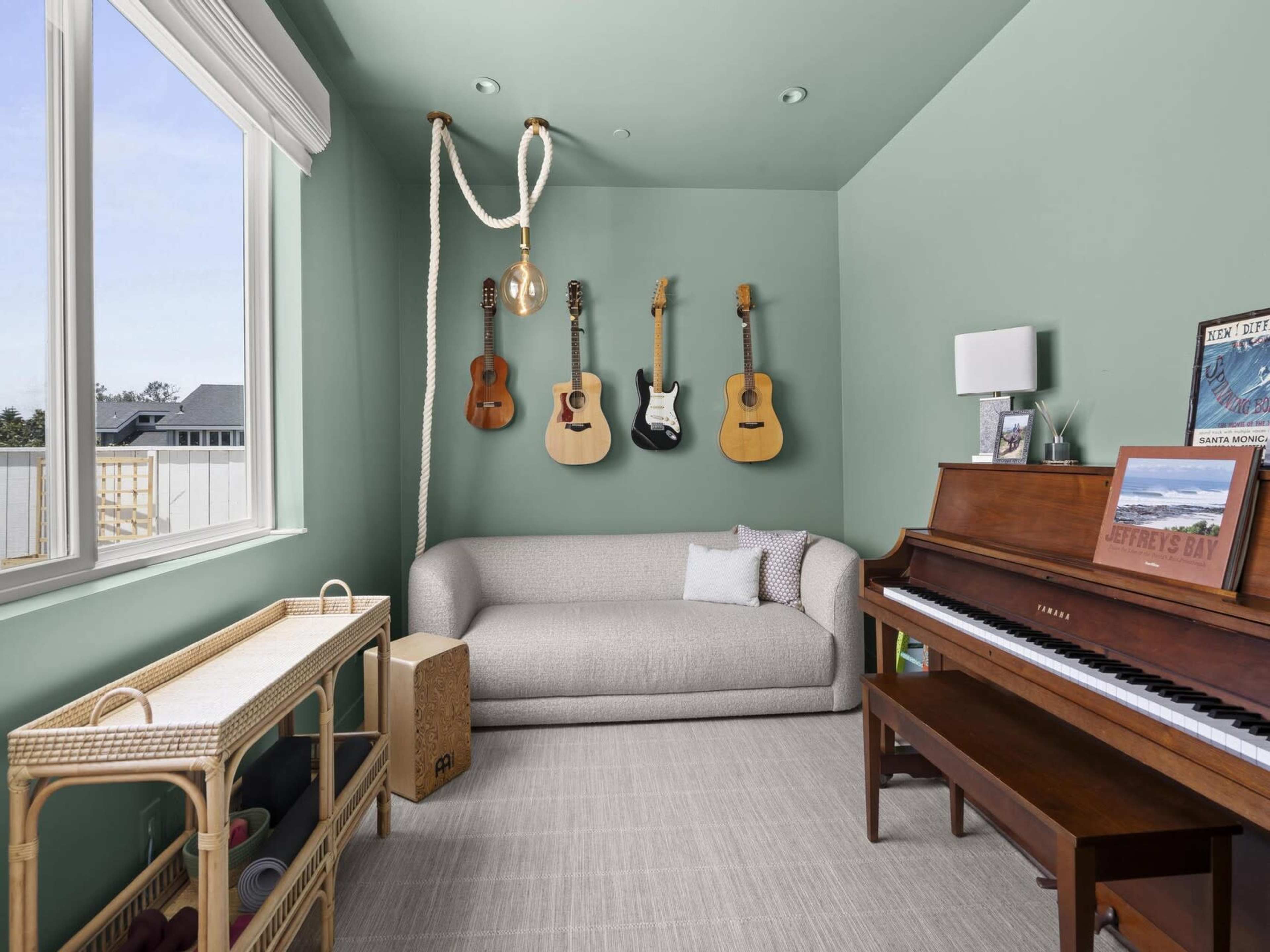 The image shows a room with a green wall featuring a couch, a piano, and hanging guitars.
