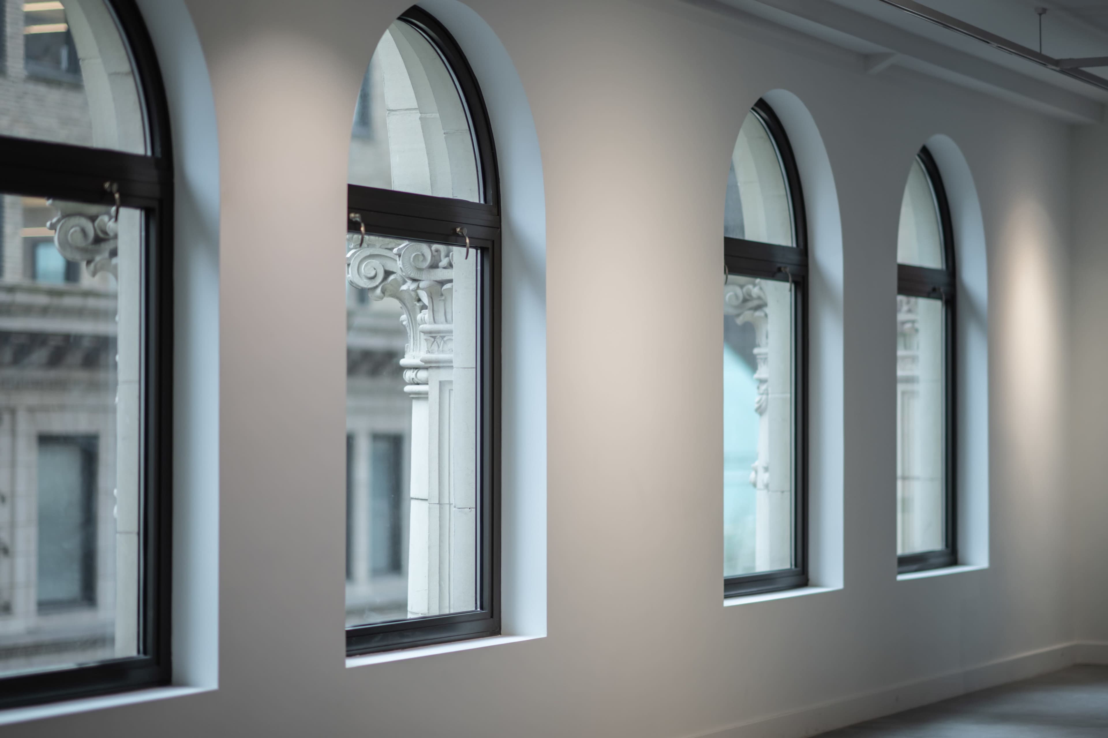 The image shows a row of three arched windows along a white wall, revealing a view of an adjacent building's architectural detail.