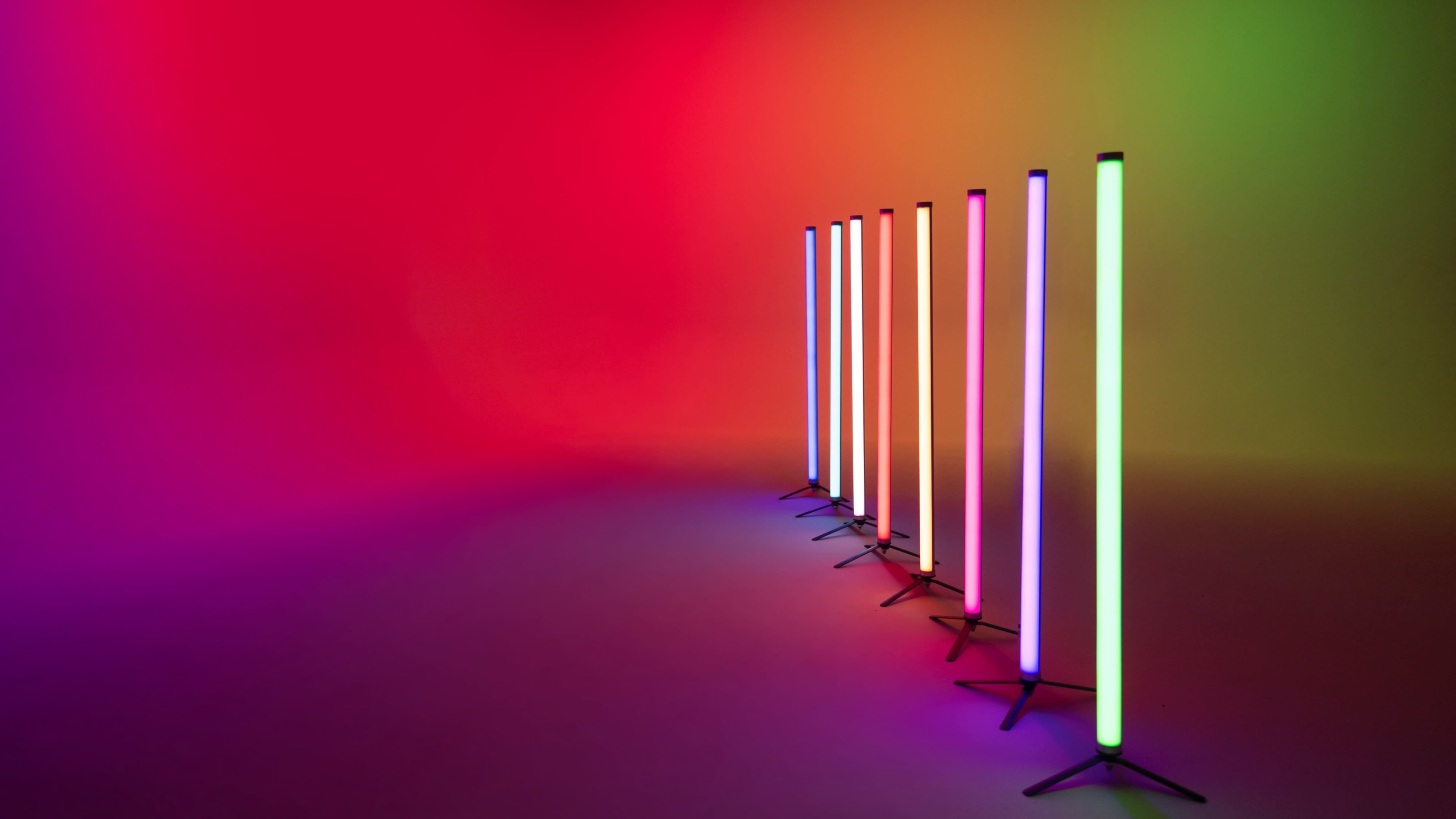 A series of illuminated vertical lights in various colors stand in a row against a vibrant, gradient background.