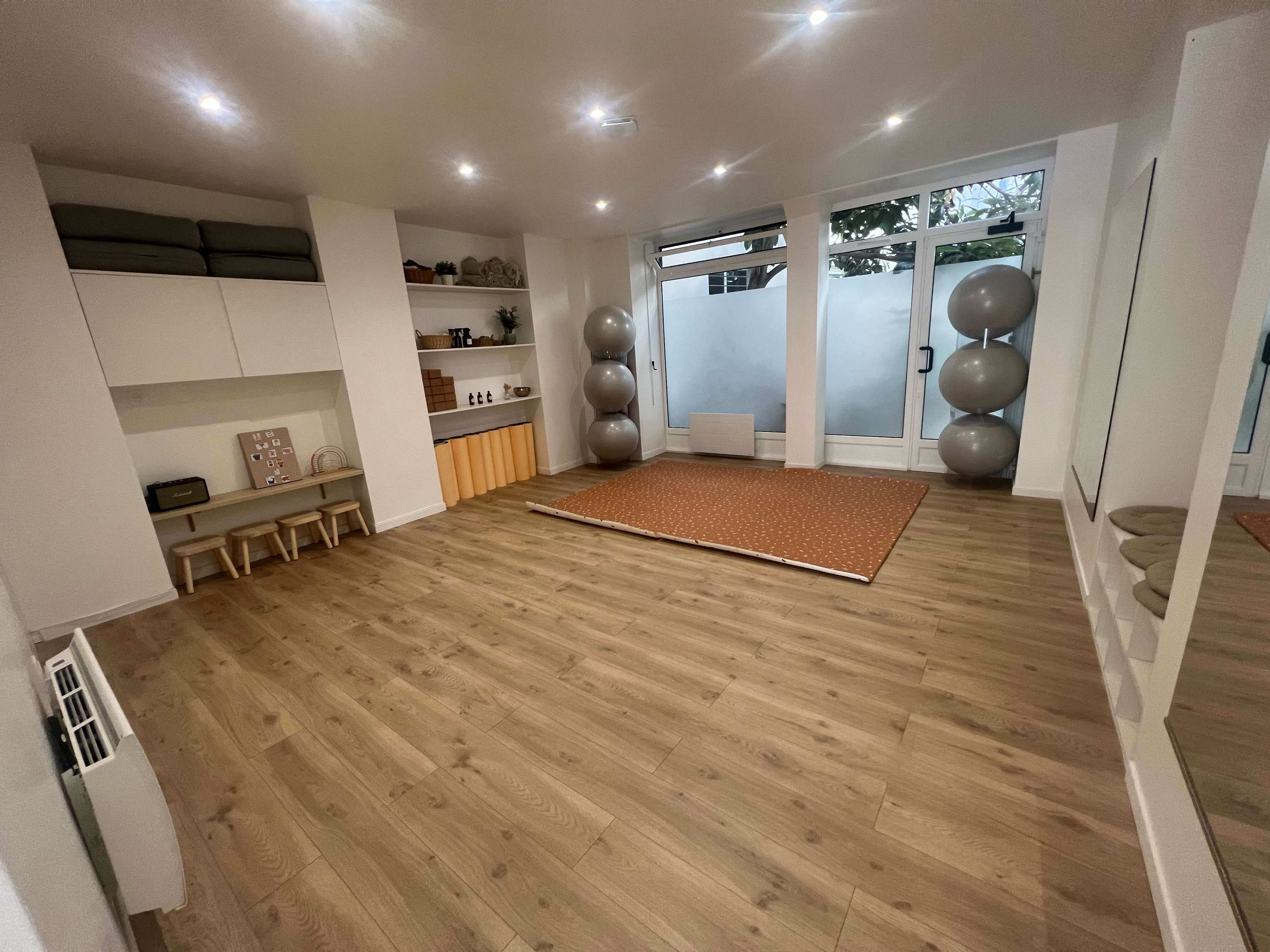 A spacious, well-lit room with wooden flooring, minimal furniture, and large windows.