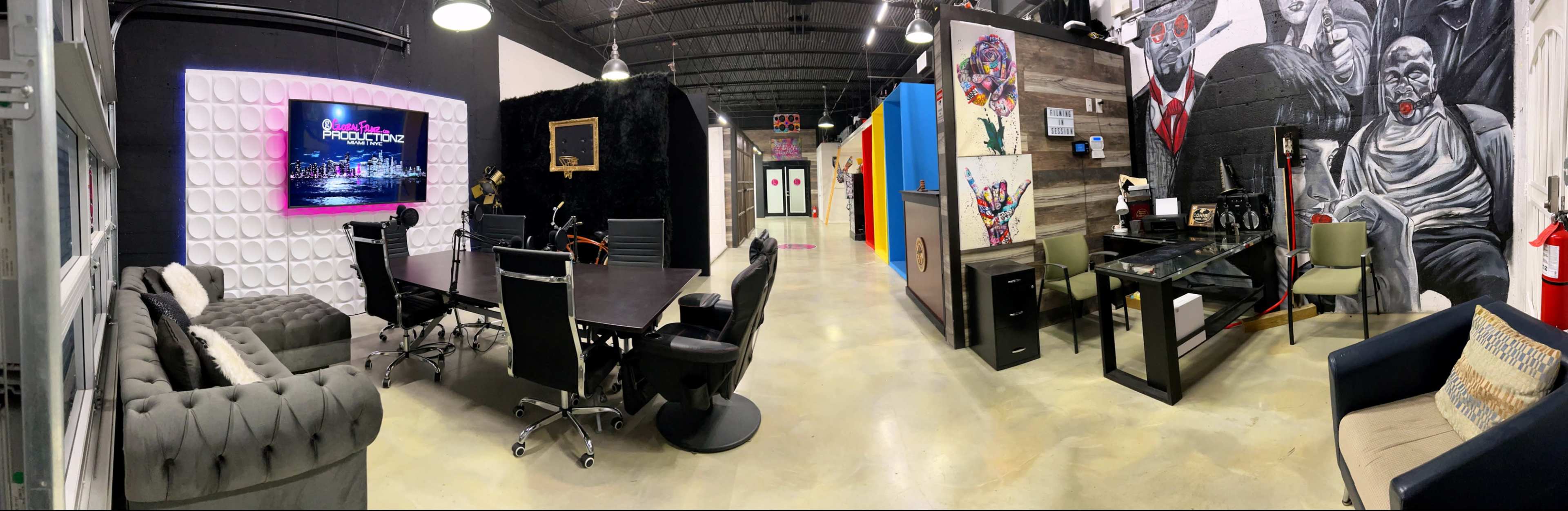 The image shows a modern coworking space featuring various workstations, a conference table, and artwork on the walls.