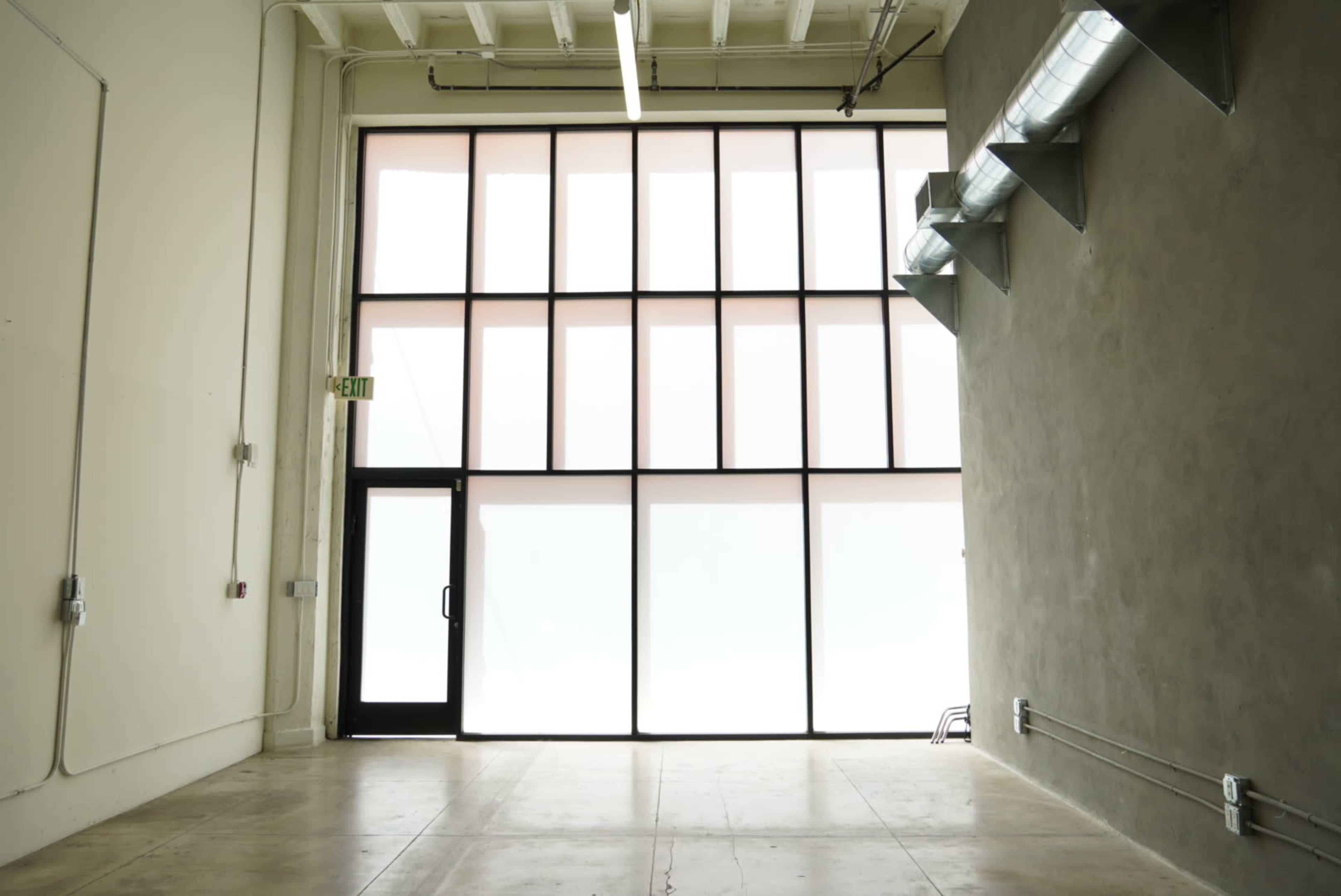 An empty interior space featuring large windows and a concrete wall.