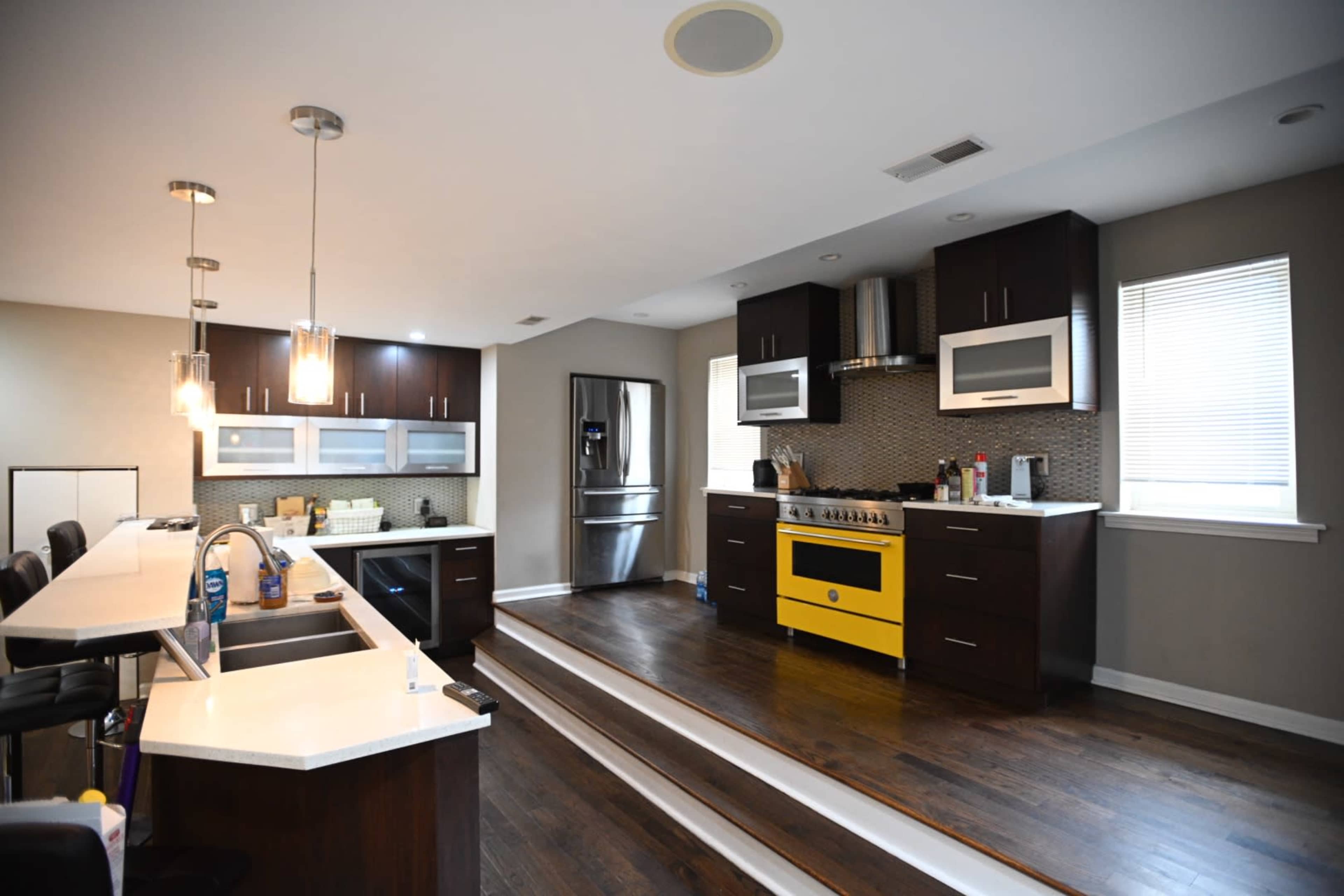 A modern kitchen features dark wood cabinets, stainless steel appliances, and a bright yellow stove, with an open layout and hardwood floors.