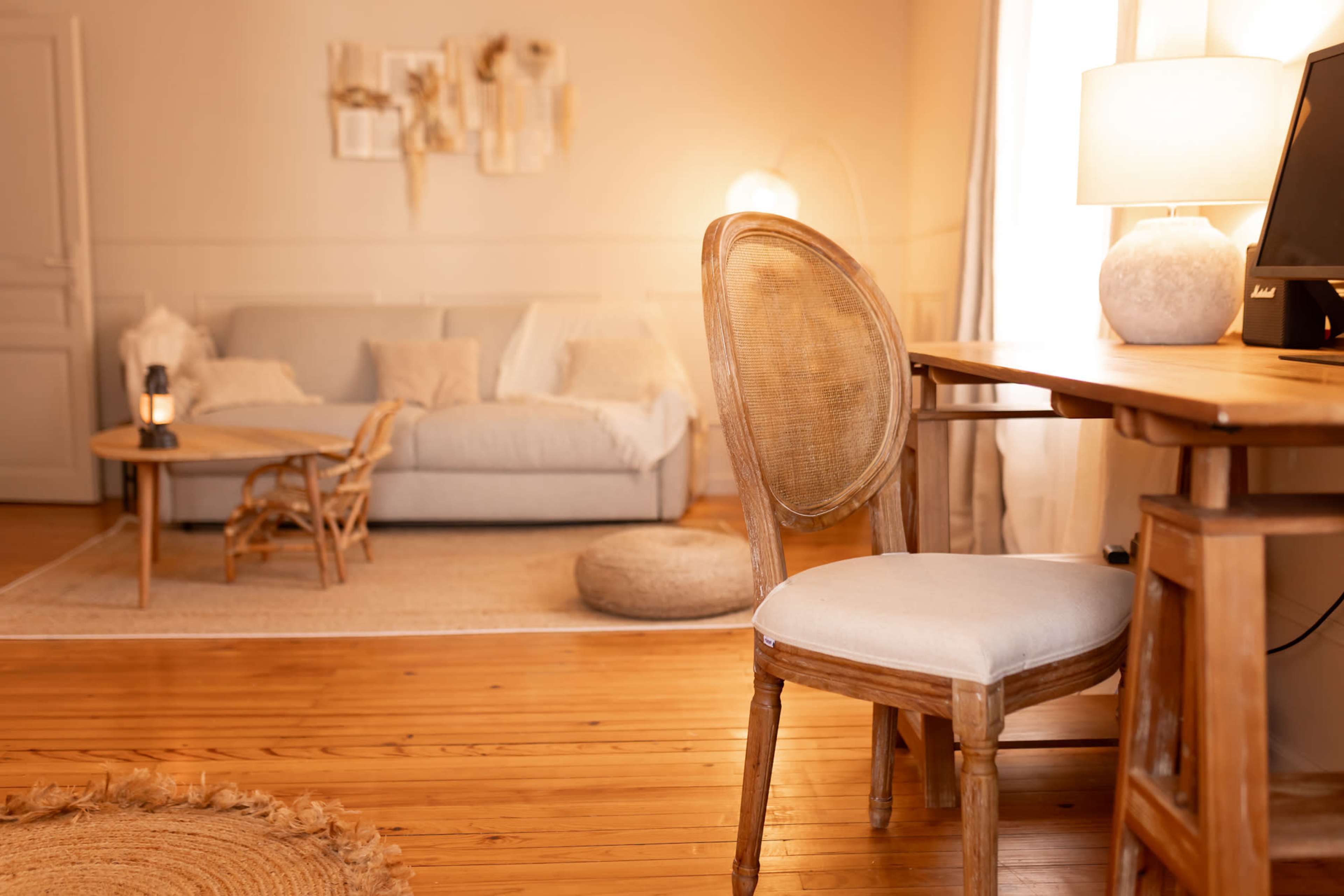 The scene features a cozy living space with a light-colored sofa, a wooden desk with a chair, and a soft area rug on a wooden floor.