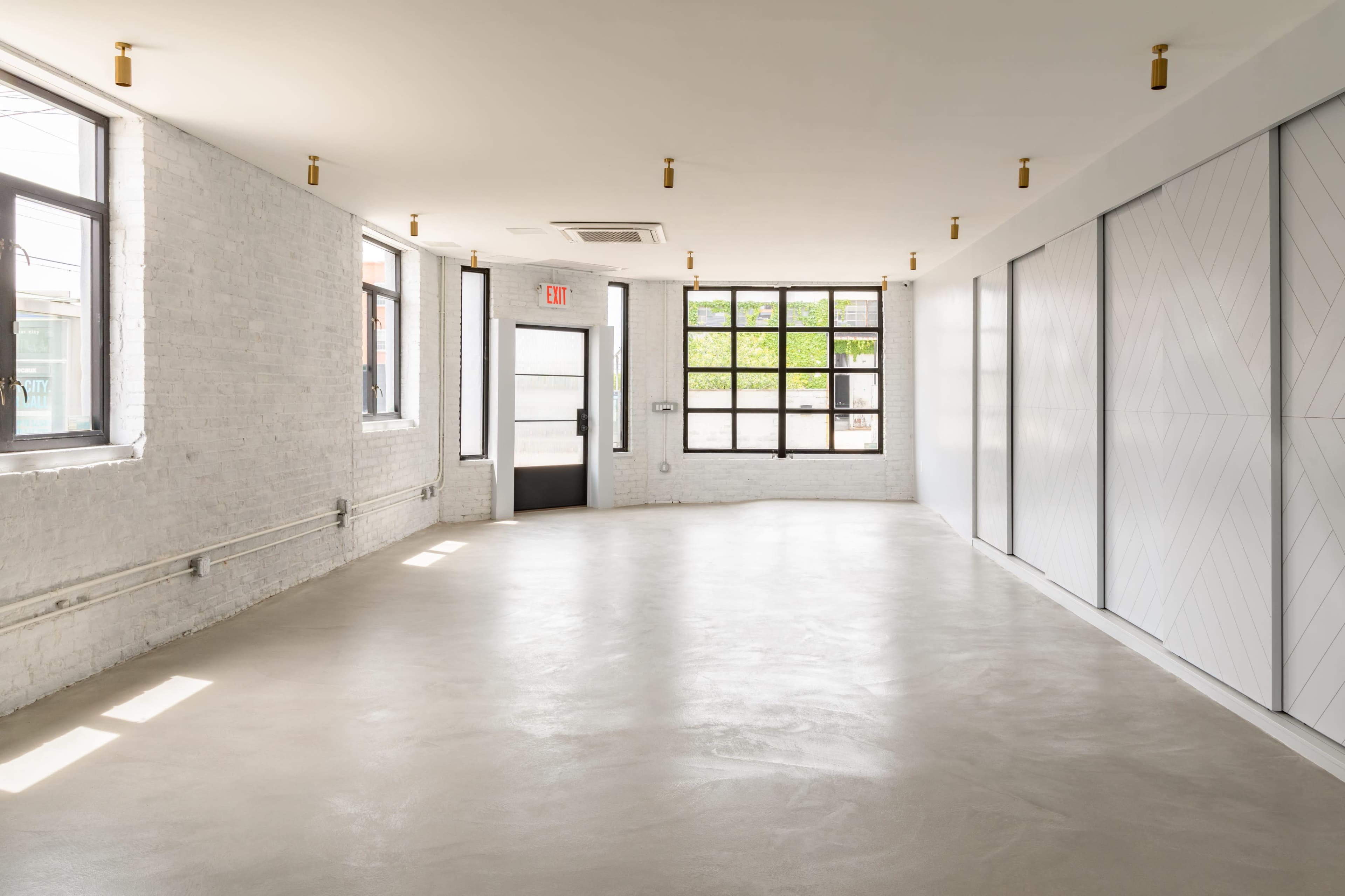 An empty room with white brick walls, large windows, and a smooth concrete floor.