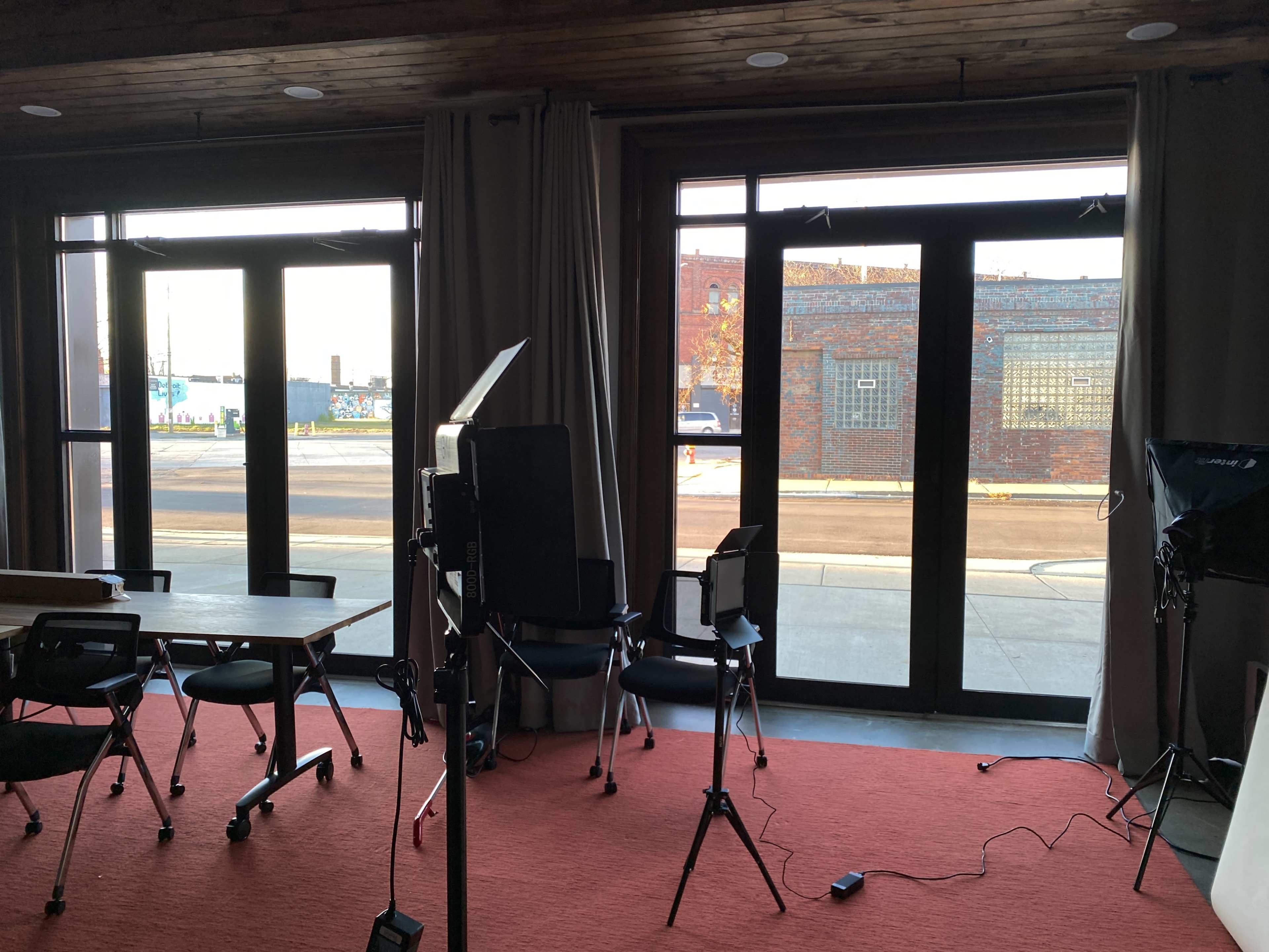 A room with a red carpet, empty chairs, and large windows that open to a street view outside.